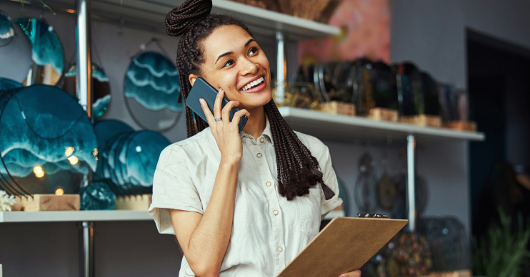 A woman holding a clipboard smiles as she talks on the phone.
