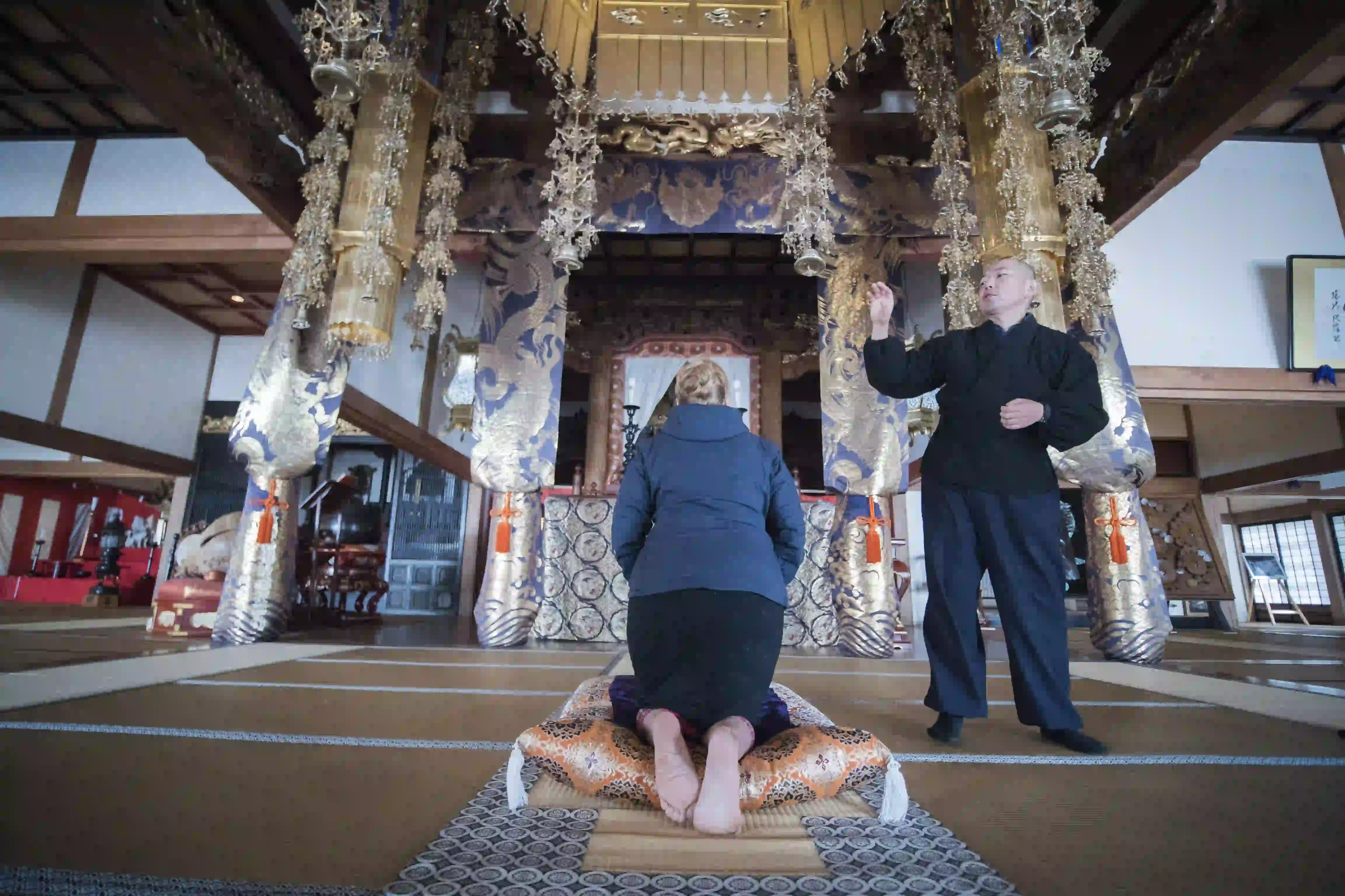 A woman kneels at an ornate temple alter and receives a blessing.