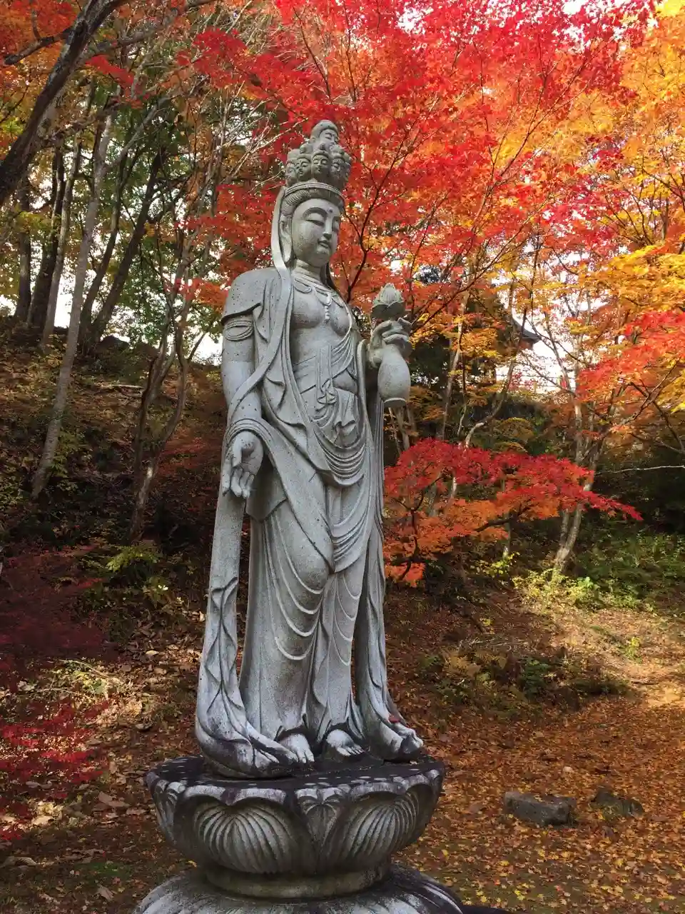 A deity statue with red Japanese maple fall leaves behind.