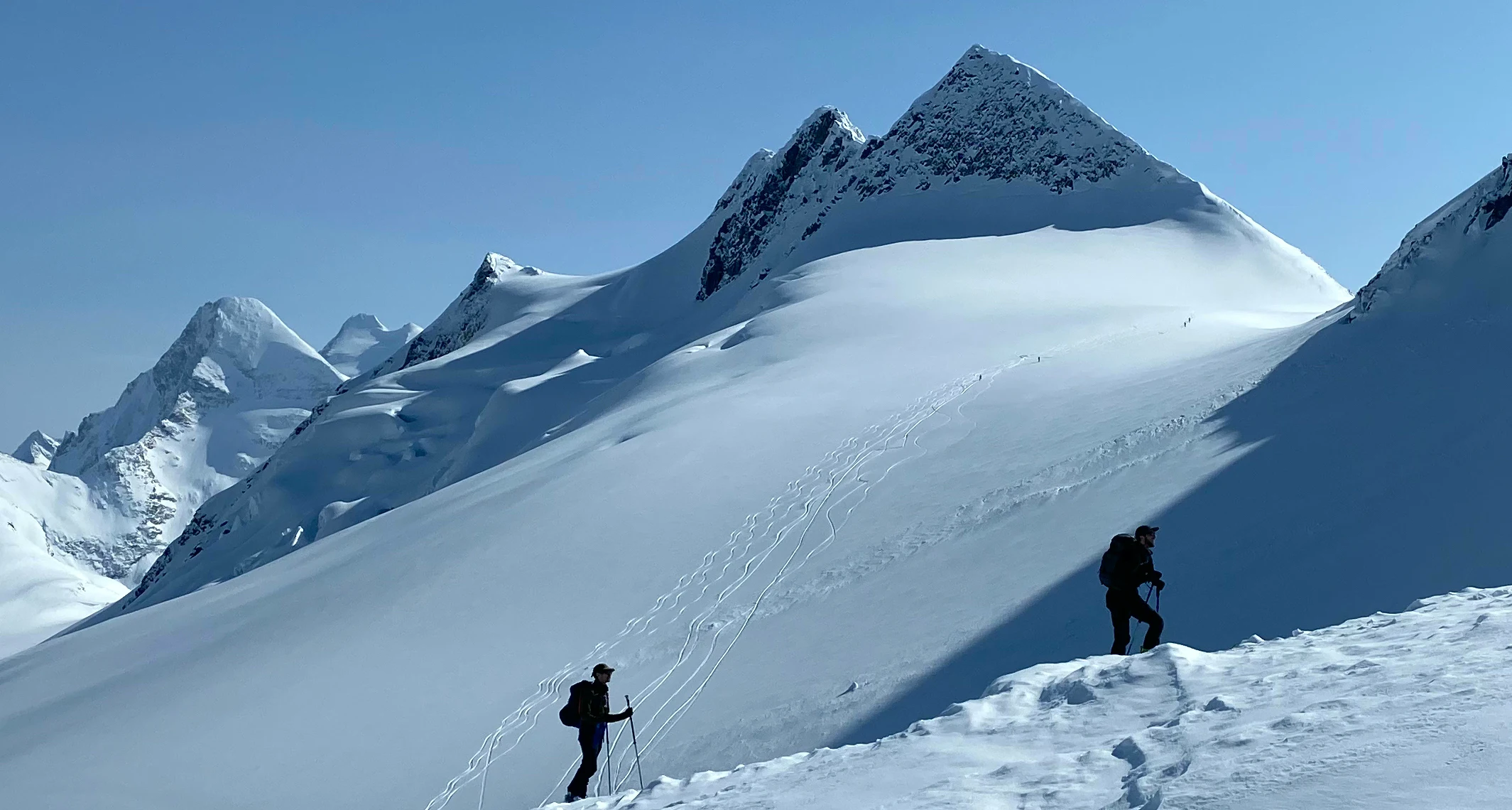 Two backcountry skiers climbing a ridge with spectacular glaciers in background