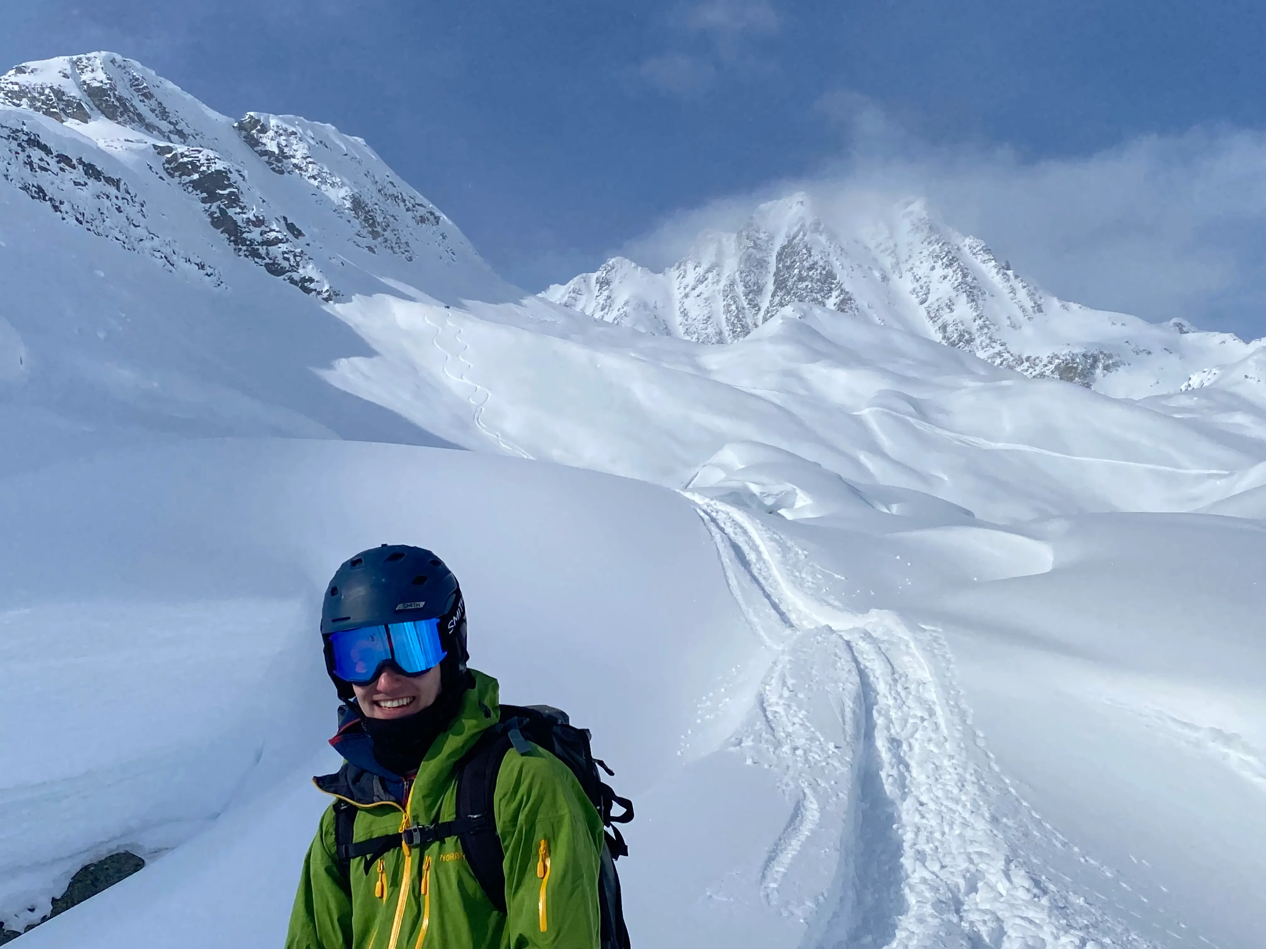 Backcountry skier in for ground, his line skied in the alpine in the background