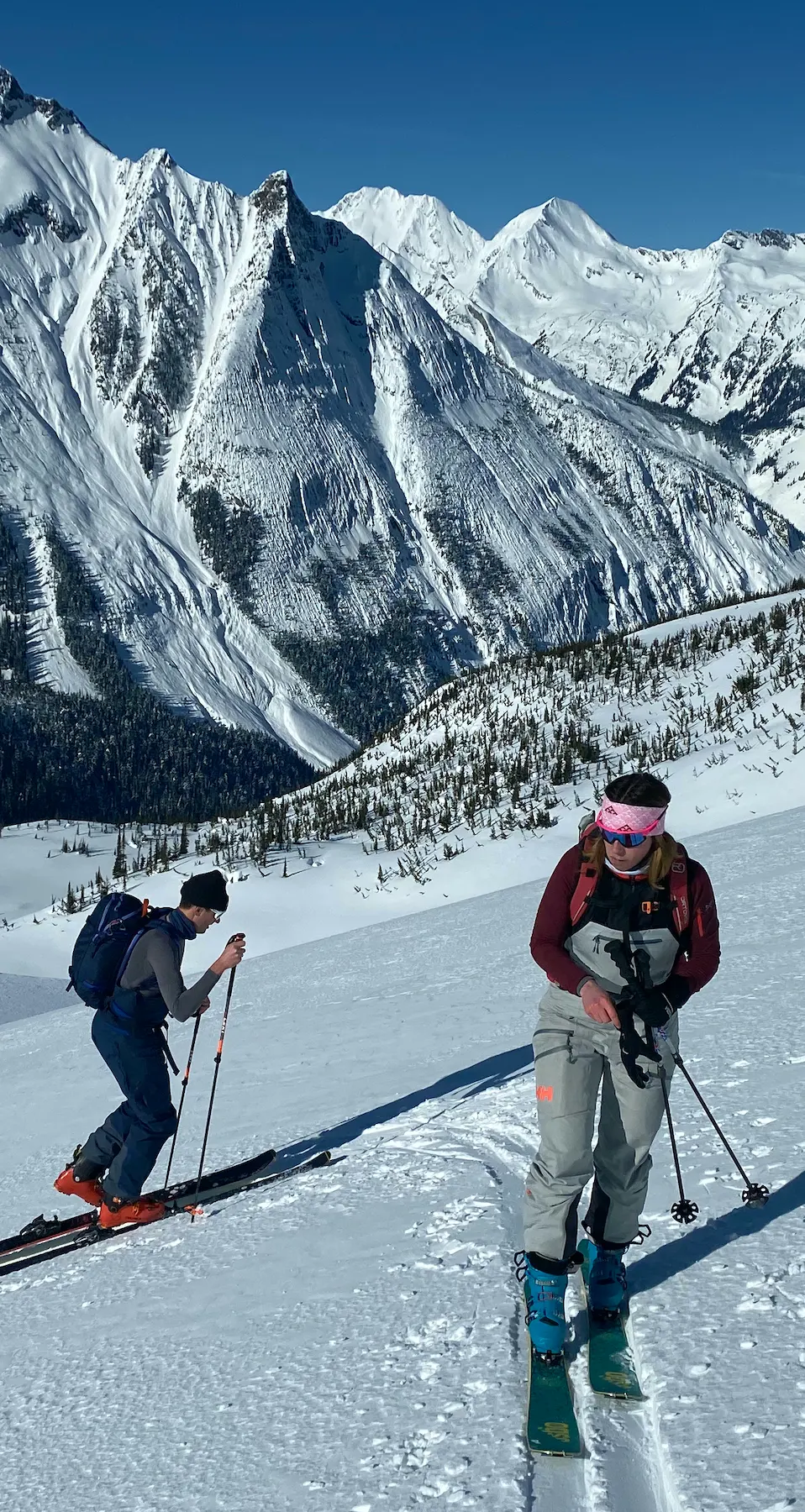 Two backcountry skiers looking casual on the trail, deep valley below