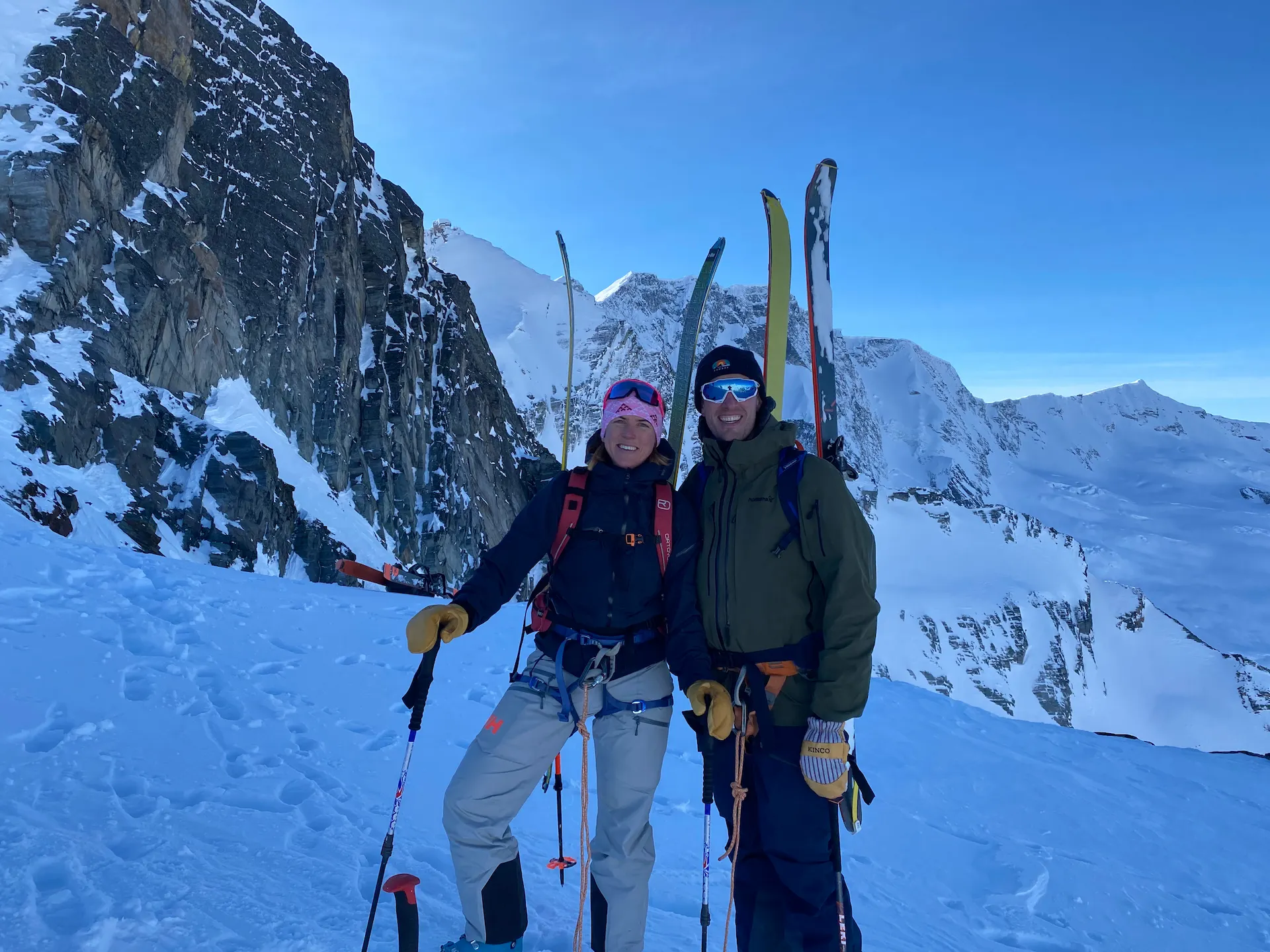 A couple after an exposed boot back, skis on pack, harness on