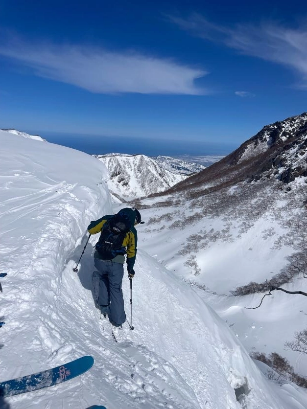 A skier perched on a steep drop in with the sea of Japan between mountains in the background