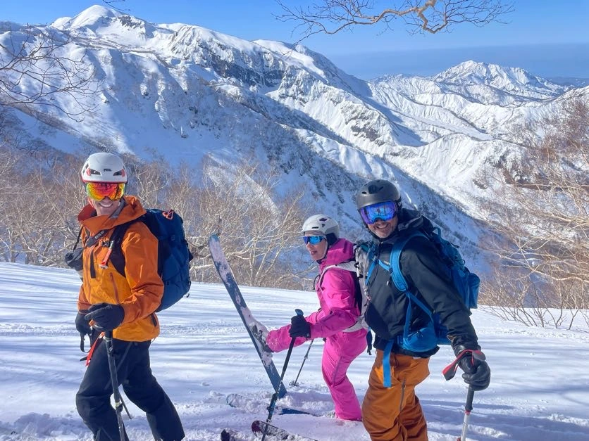Three smiling skiers with big mountain views in the background