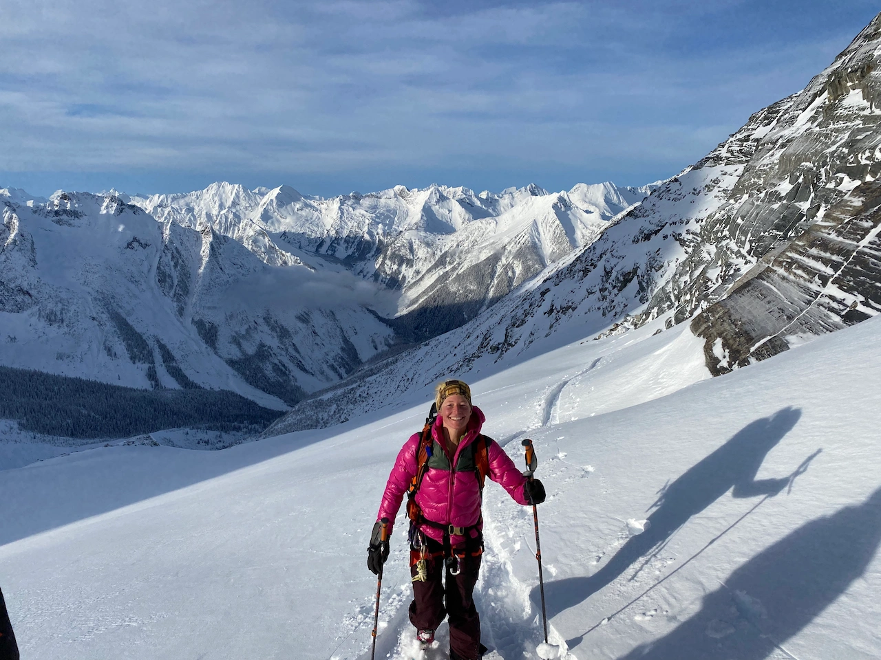 A woman ski touring with a big grin and large mountains the background 
