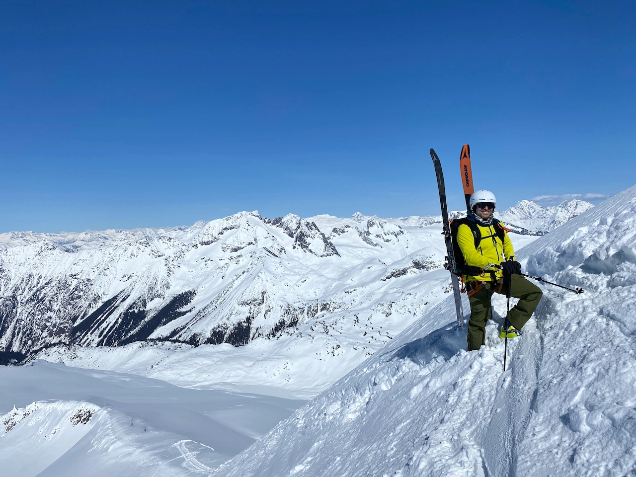 A single skier stands on a high peak with skis on pack