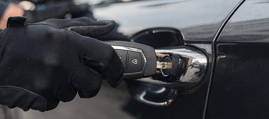 Hand mit schwarzem Handschuh steckt Autoschlüssel in Türgriff eines schwarzen Autos.