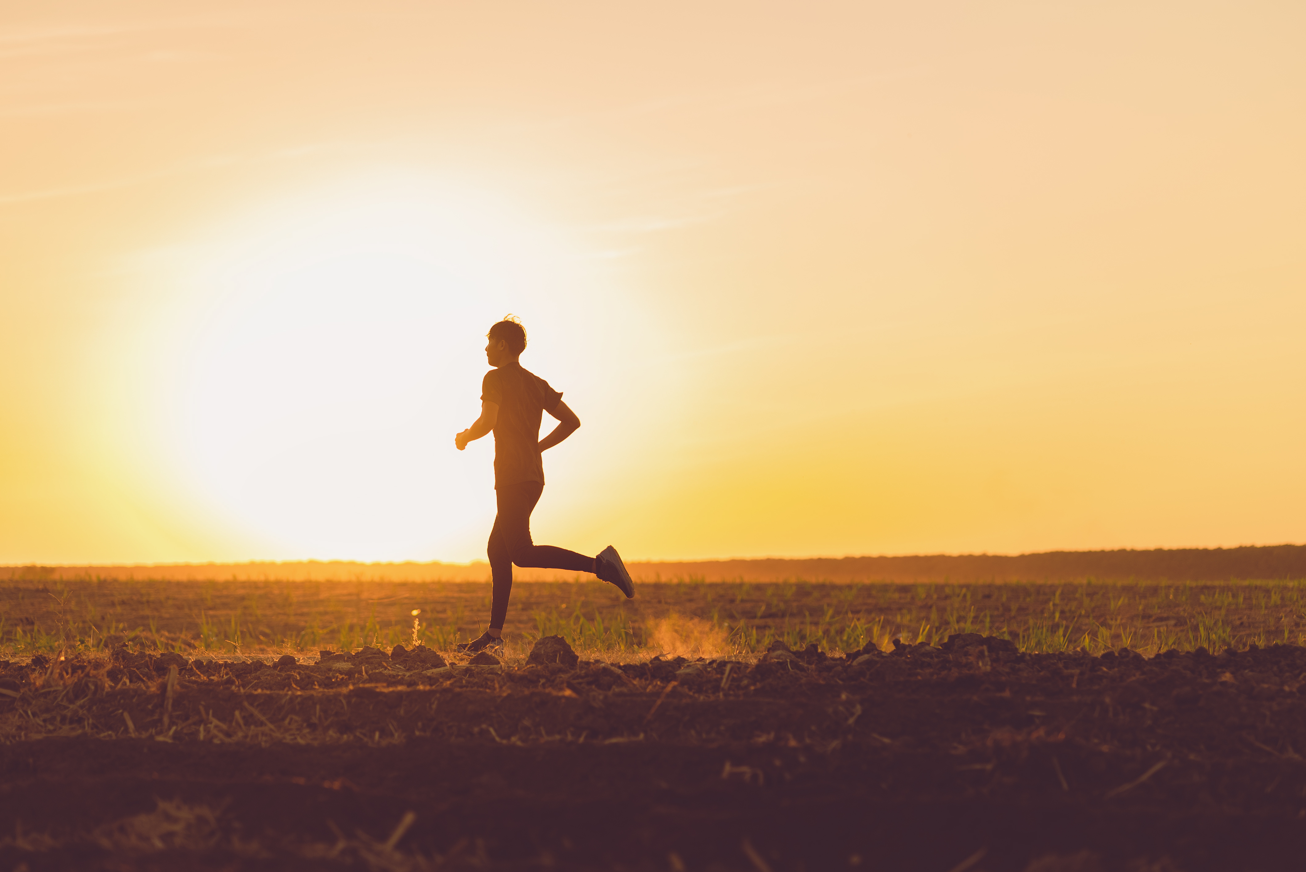 A person running across a field at sunset