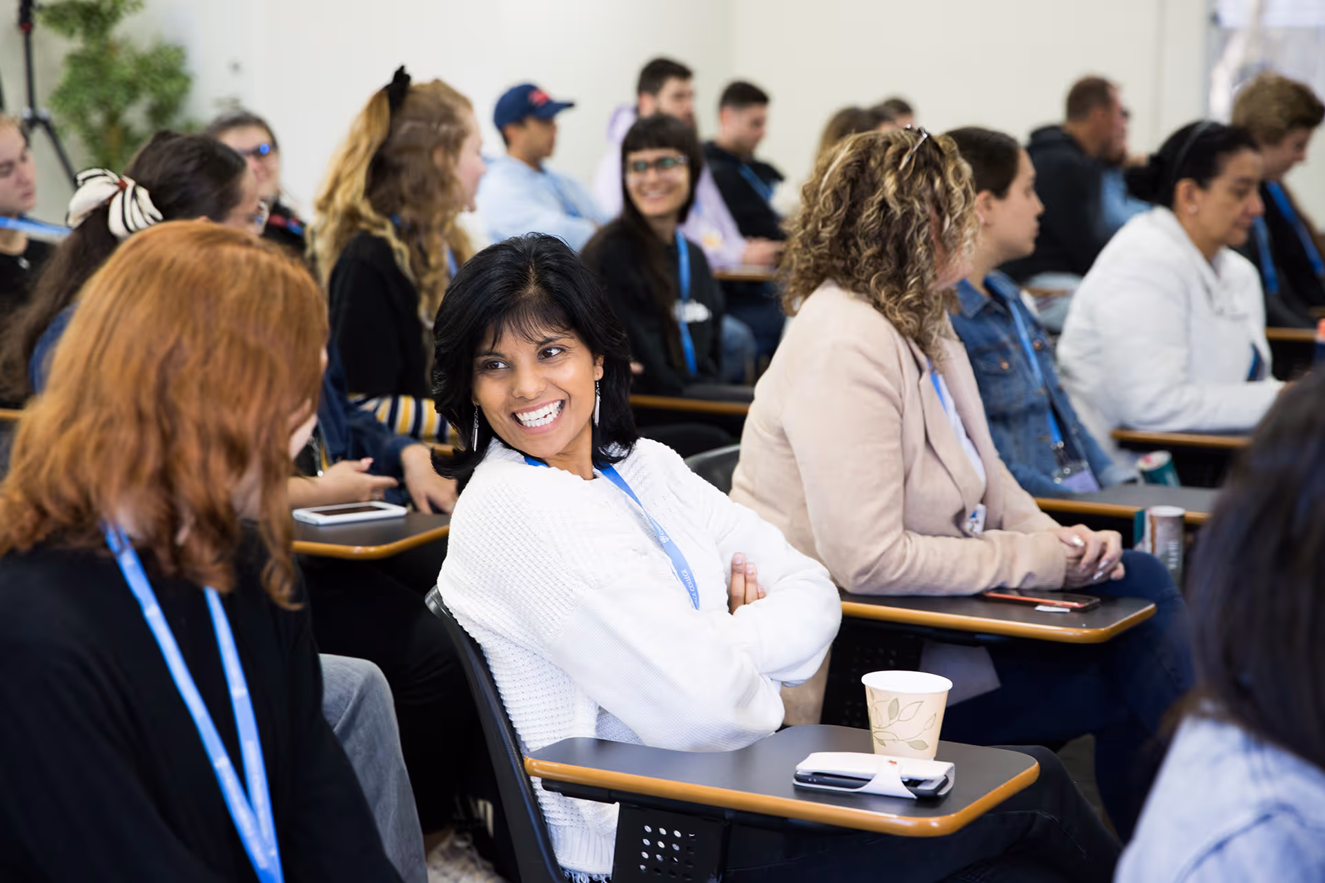 Diverse group of adults seated in a classroom, engaging in conversation and smiling.