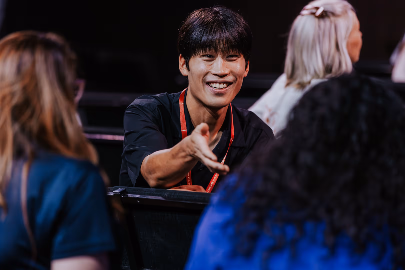 Smiling man with dark hair reaching out his hand to greet or shake hands with two women facing him.