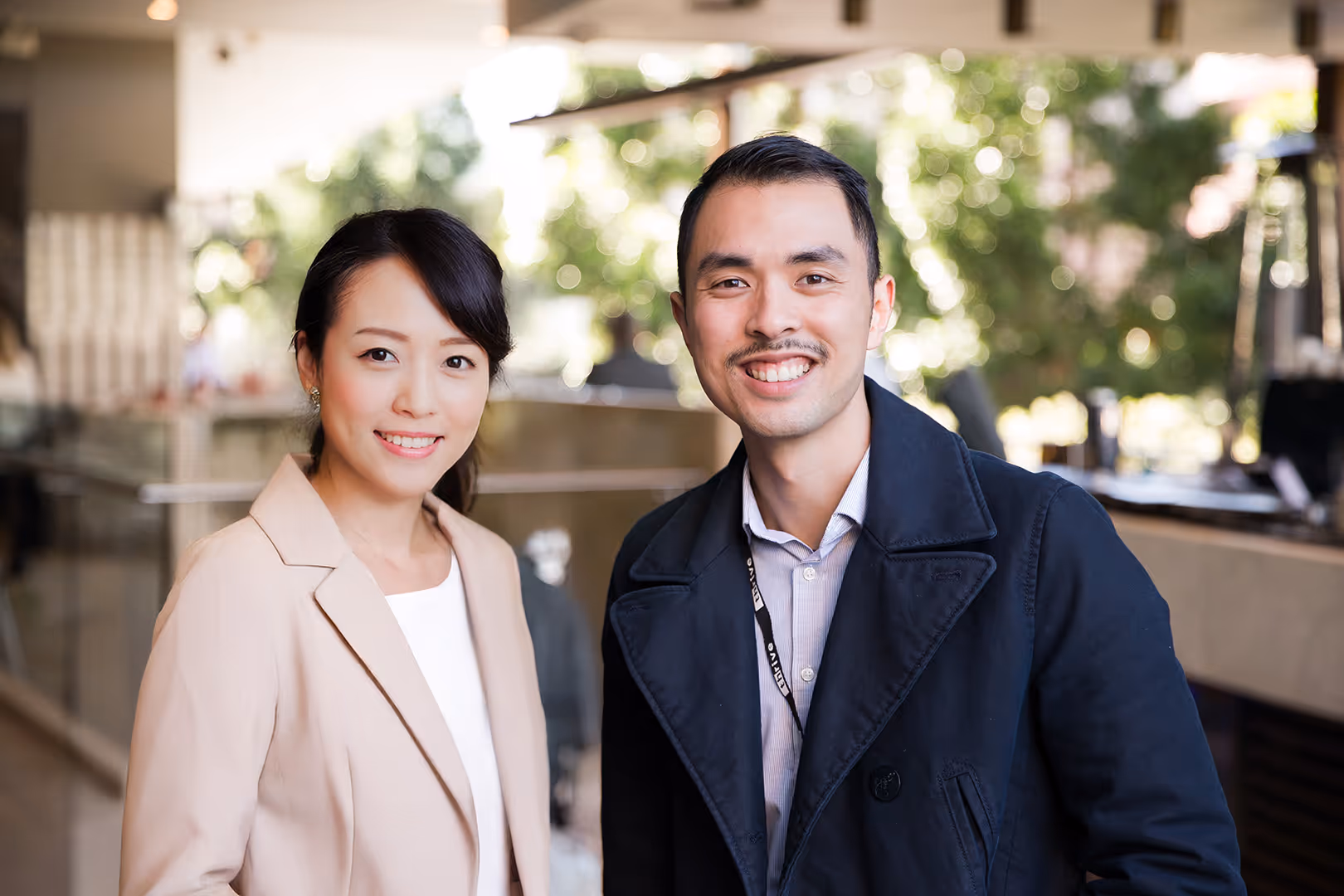 Smiling Asian man and woman standing together in a bright indoor setting with blurred background.