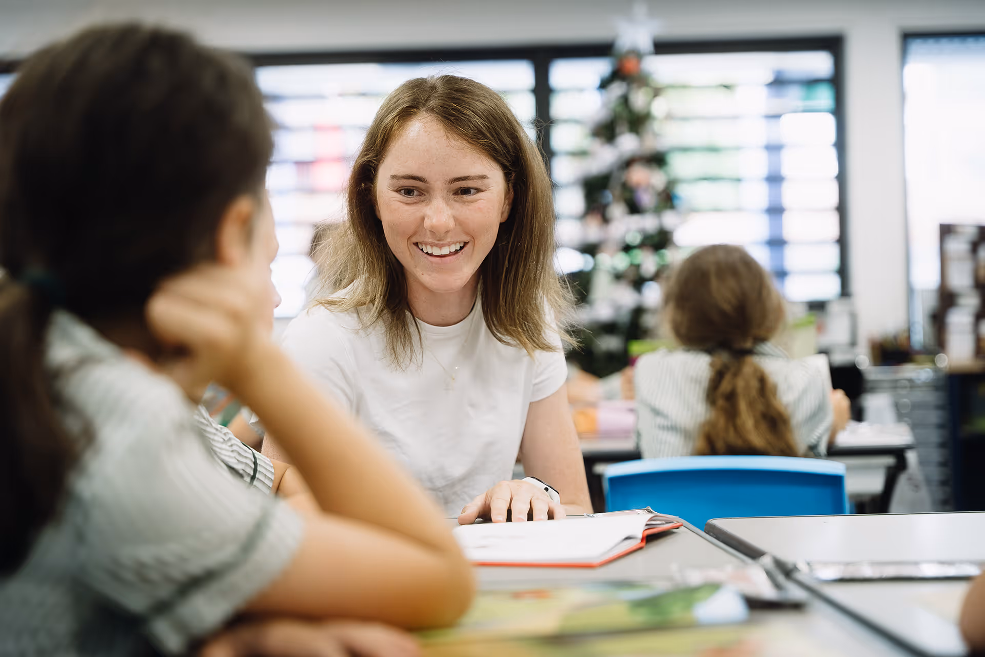 Smiling female teacher interacting with students in a classroom setting.