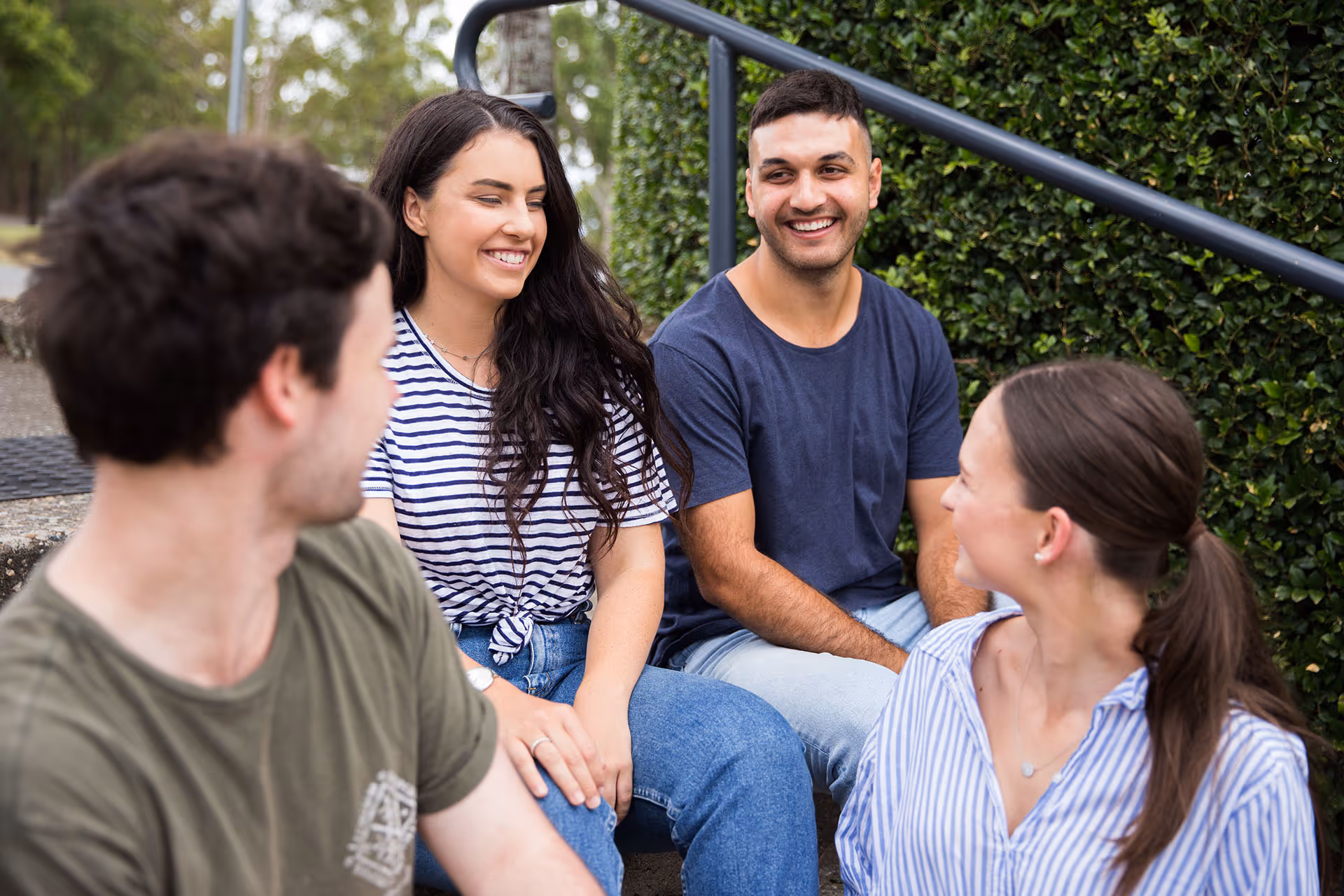Four young adults sitting outside on steps, smiling and engaged in conversation.