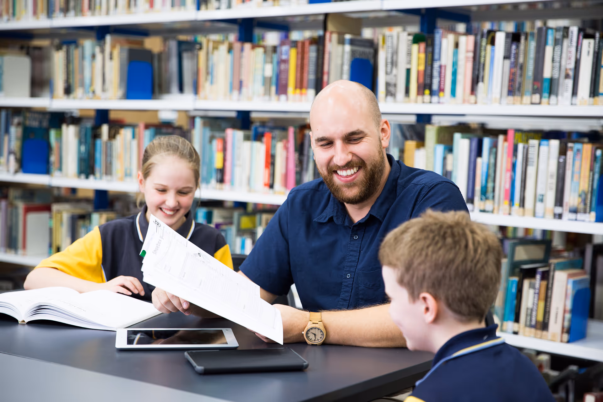 Teacher and two students engaging in a cheerful study session in a library.