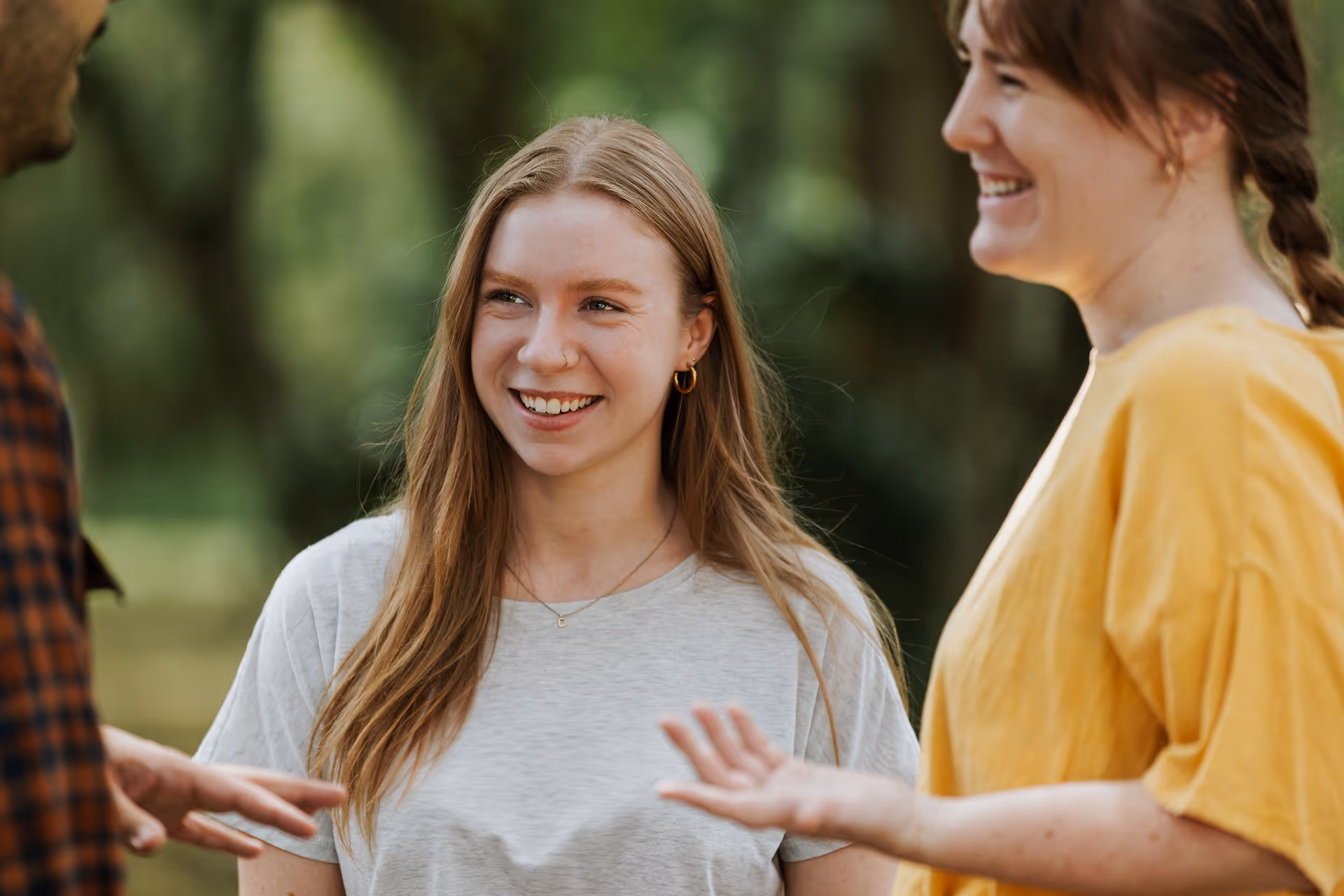 Three young adults outside smiling and engaging in conversation with a blurred green background.