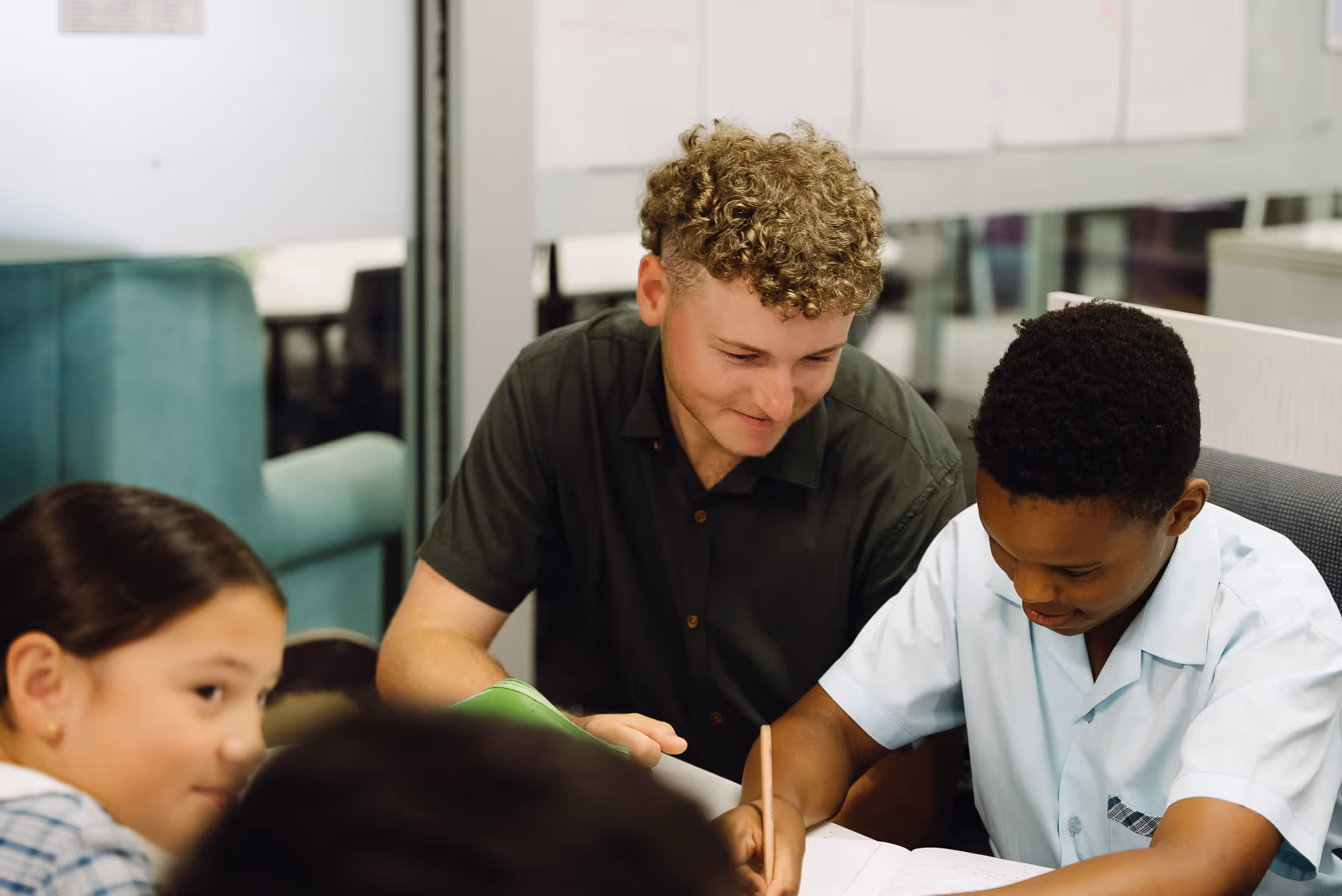 Adult male tutor helping a student with schoolwork while other children sit nearby.