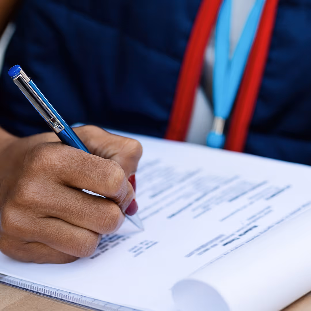 Close-up of a person holding a blue pen and writing on a white document with printed text.