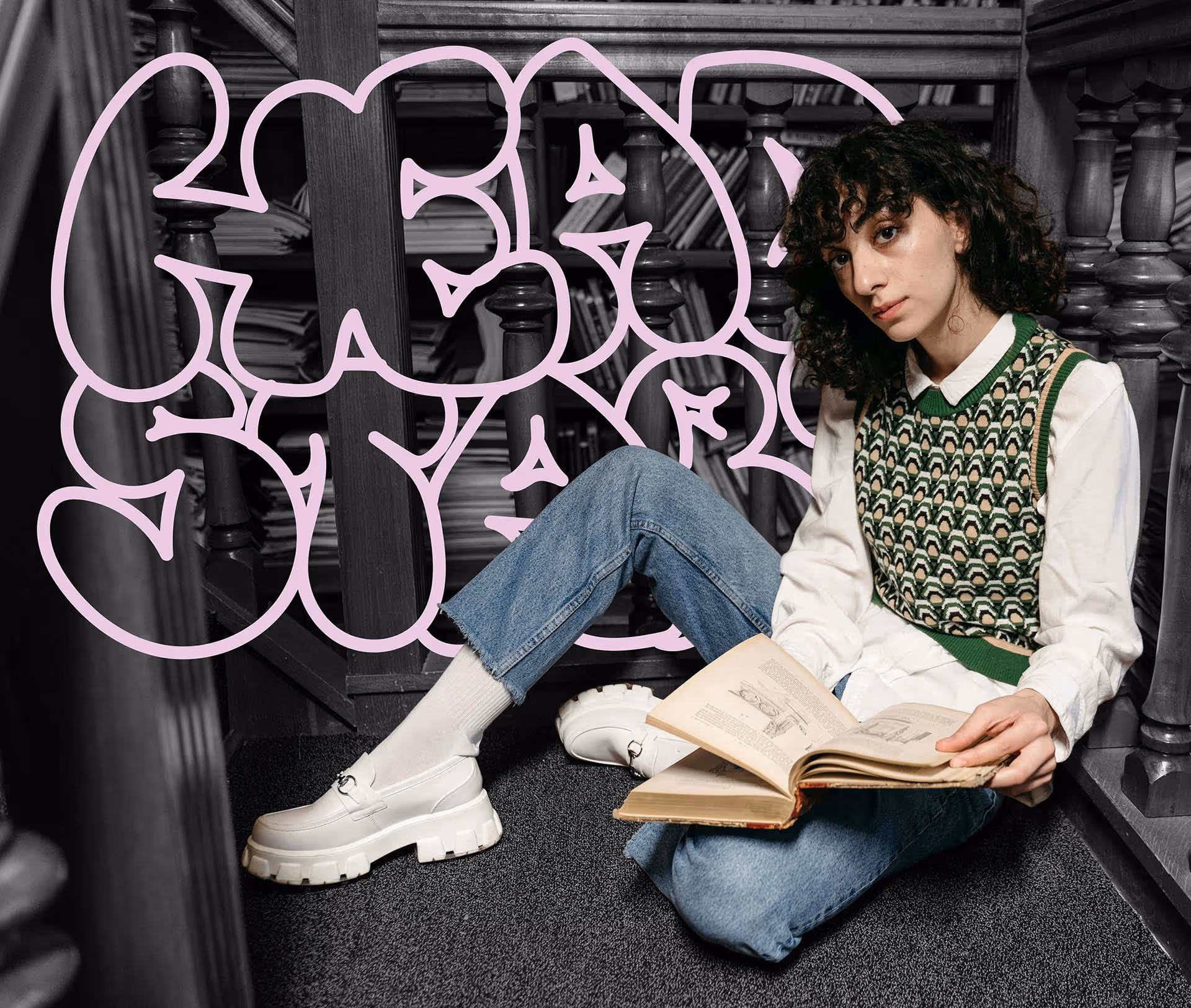 Person with curly hair sitting on carpeted floor between wooden railings, reading an open book with a retro green patterned vest and white shirt.