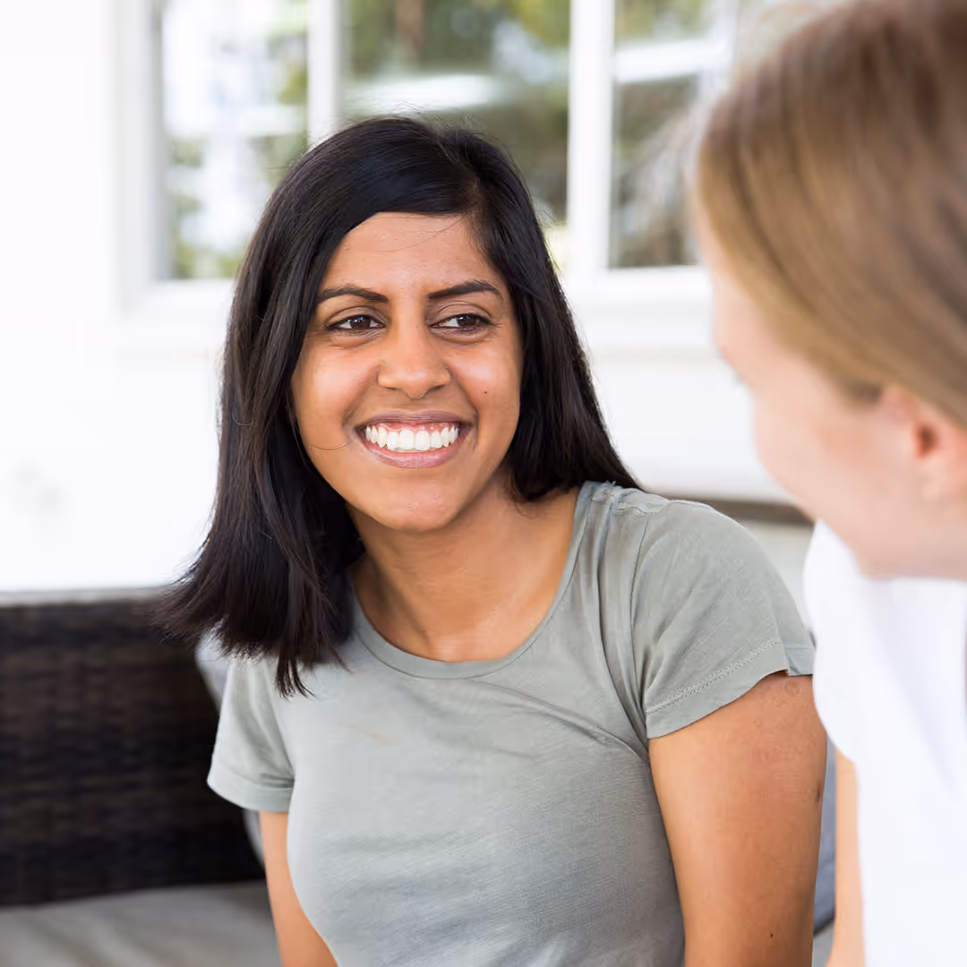 Smiling young woman with dark hair looking at another person during a conversation in a bright indoor space.