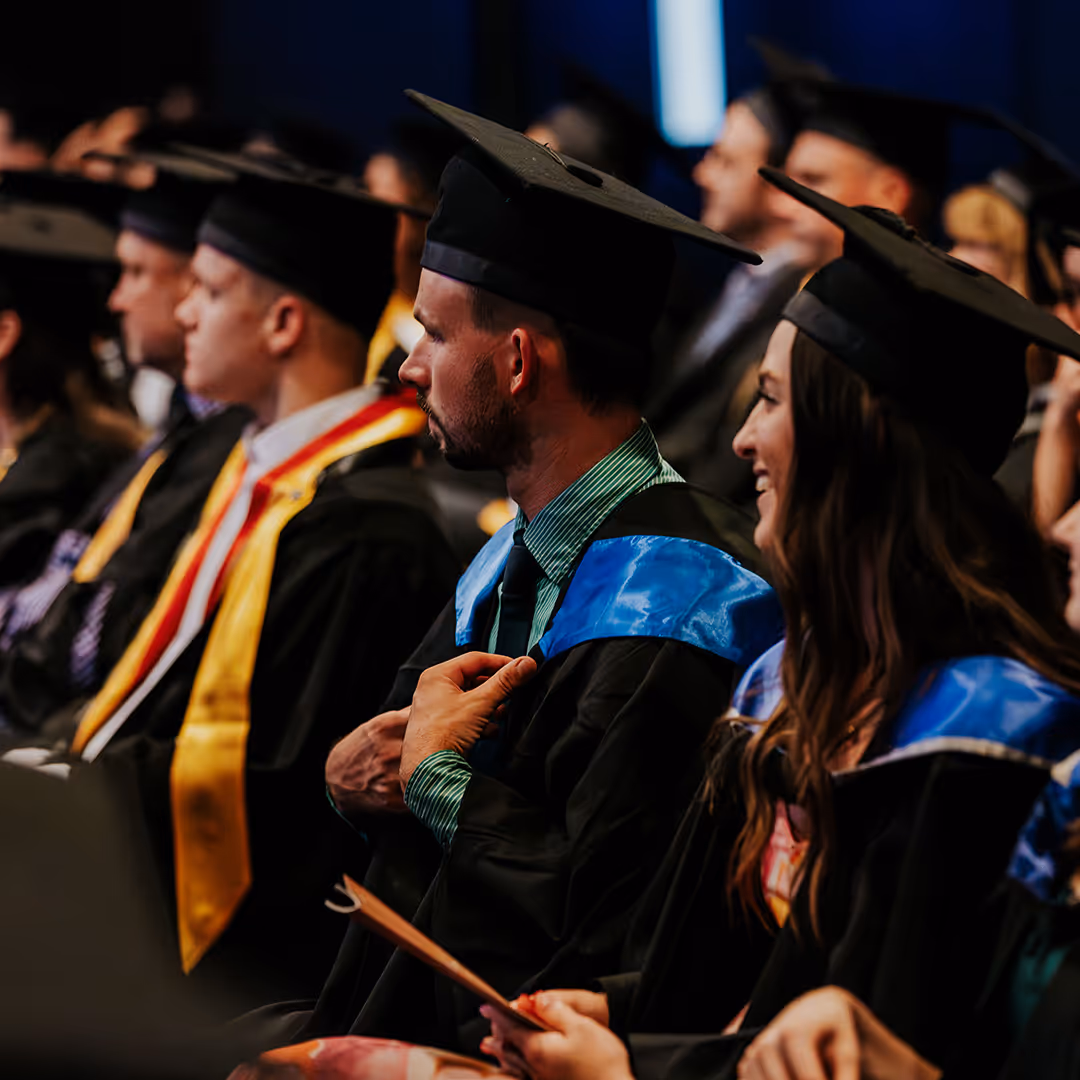 Graduates in caps and gowns seated in a row during a graduation ceremony.