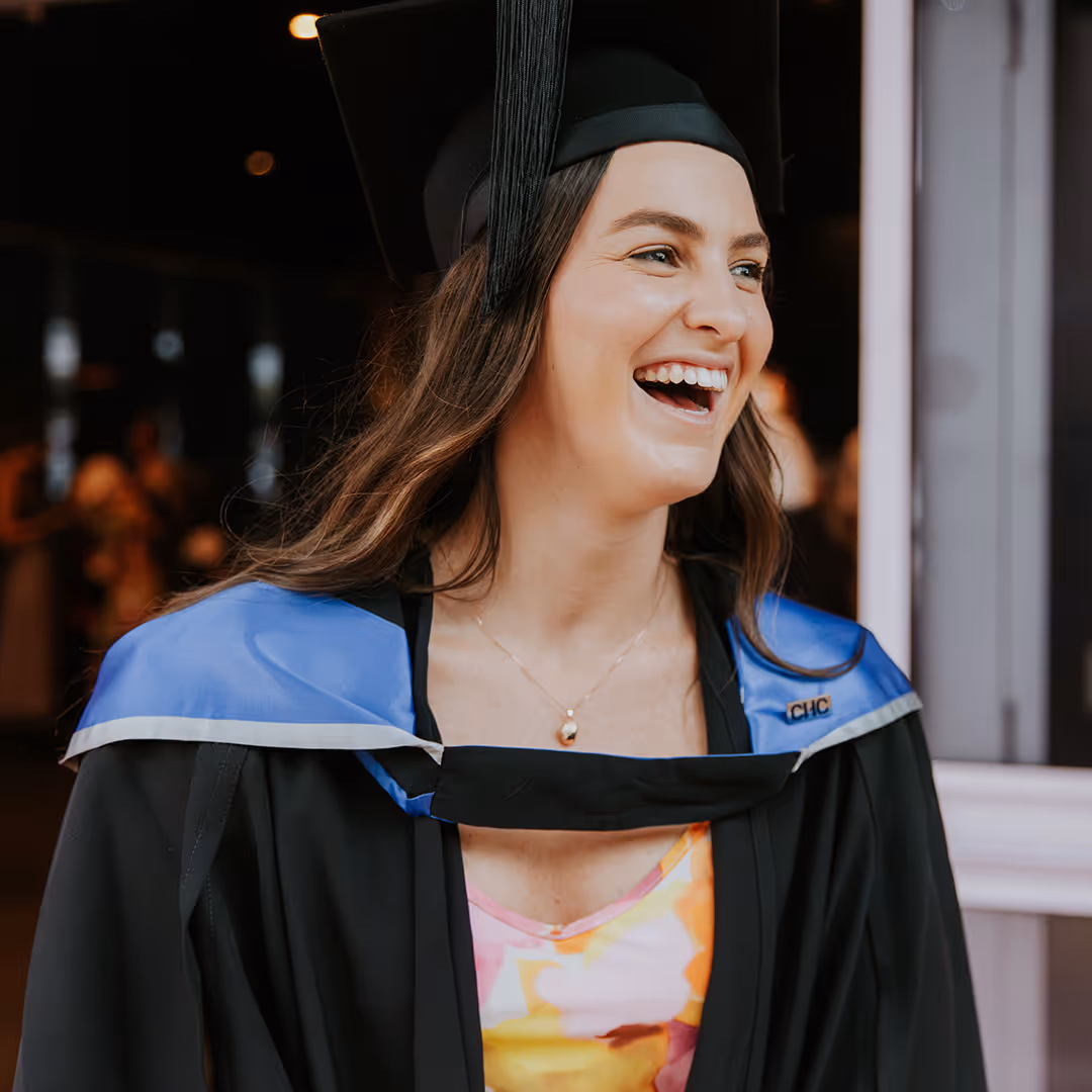 Smiling woman in graduation cap and gown with blue stole, wearing a colorful dress underneath.