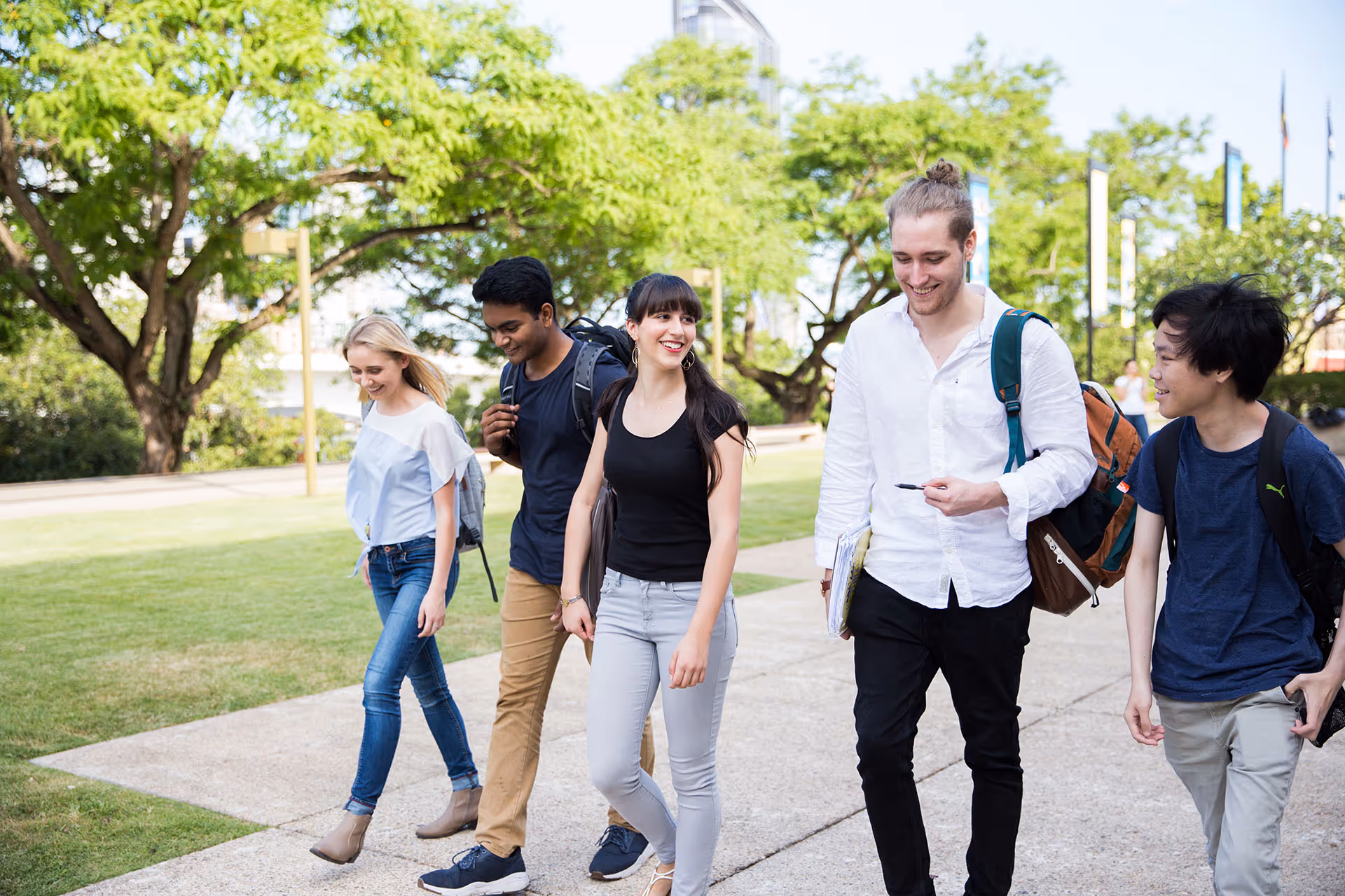 Group of five diverse young adults walking and talking outdoors on a sunny day.