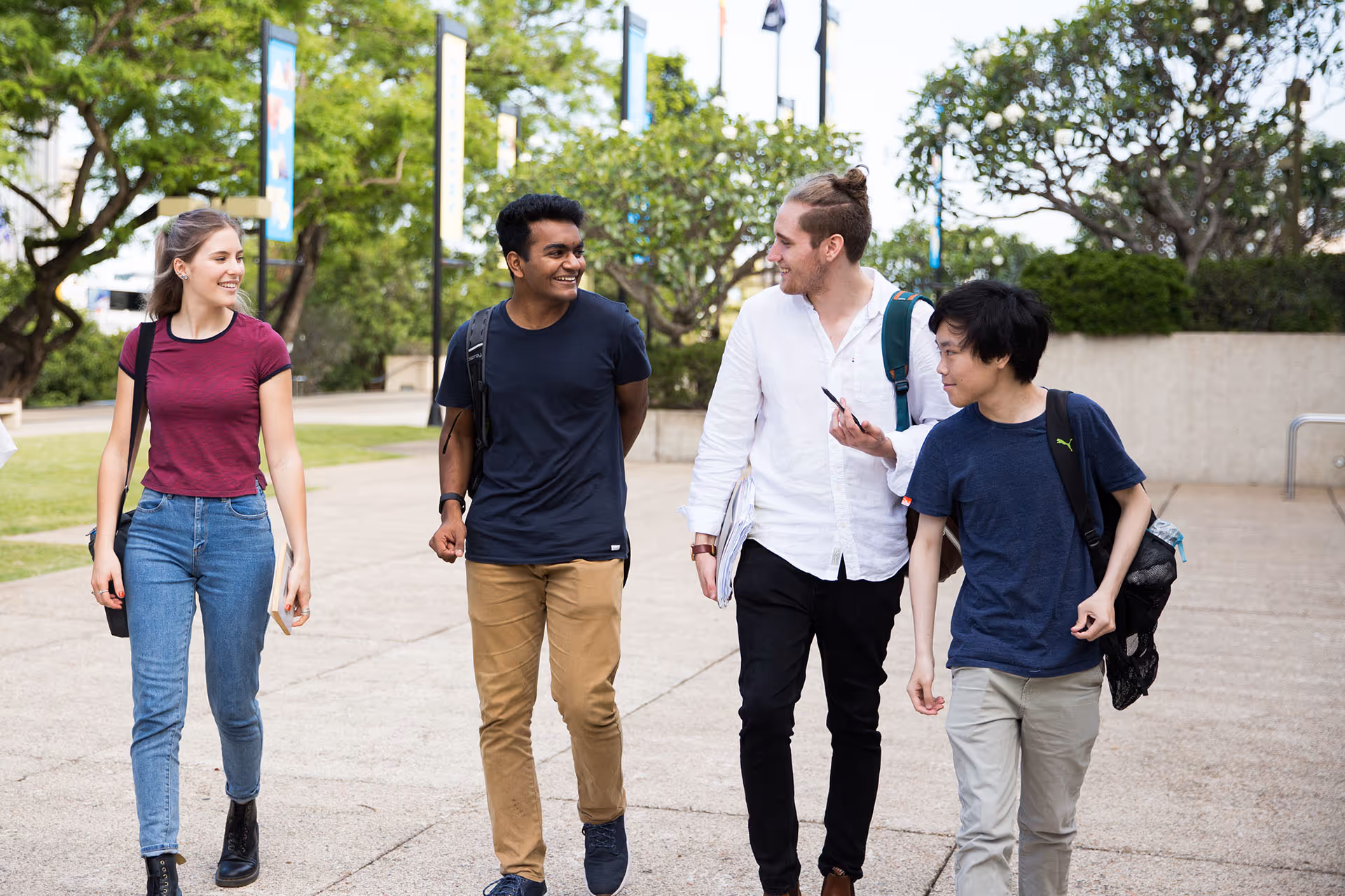 Four diverse young adults walking outside on a university campus, smiling and chatting.