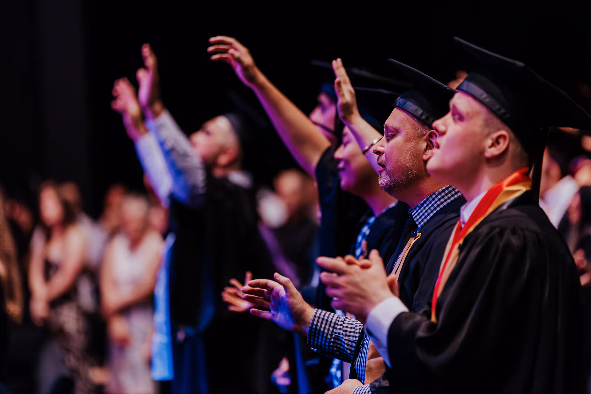 Graduates wearing caps and gowns, raising hands and clapping during a ceremony.