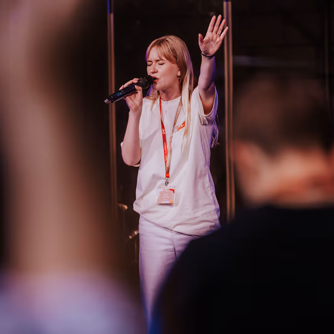 Woman with blonde hair singing into a microphone with eyes closed and one hand raised.