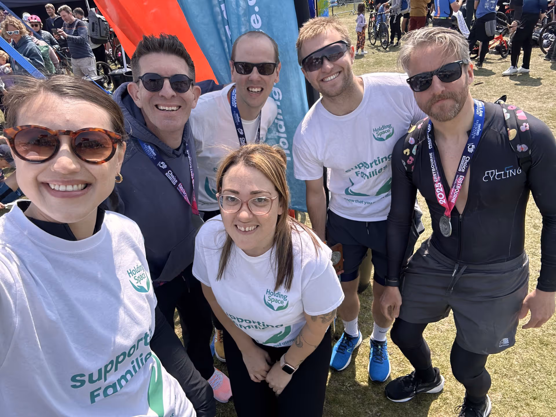 A group of six people wearing medals and charity shirts pose together outside at an event.