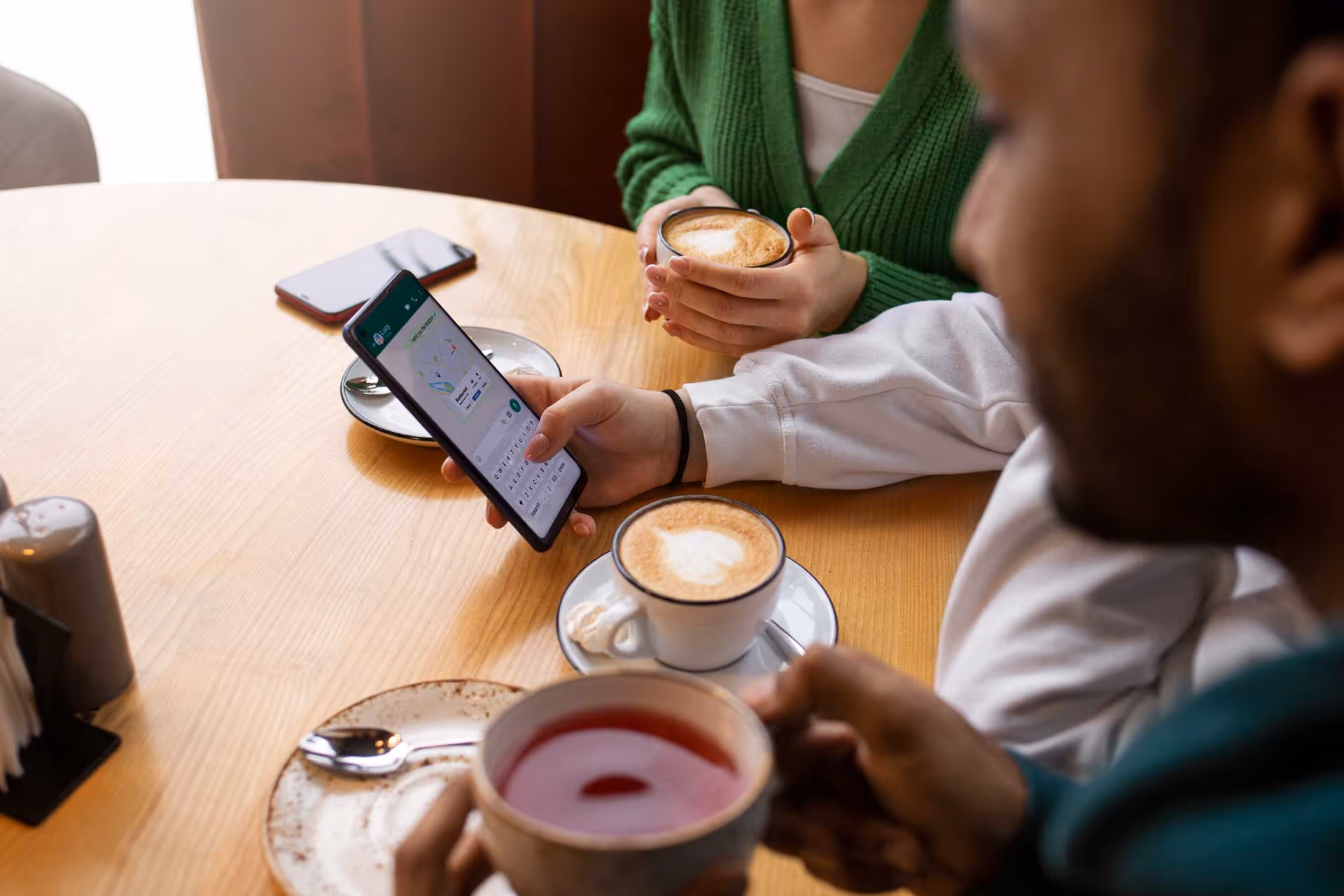 Two people sitting at a table, drinking coffee. One is looking at a smartphone.