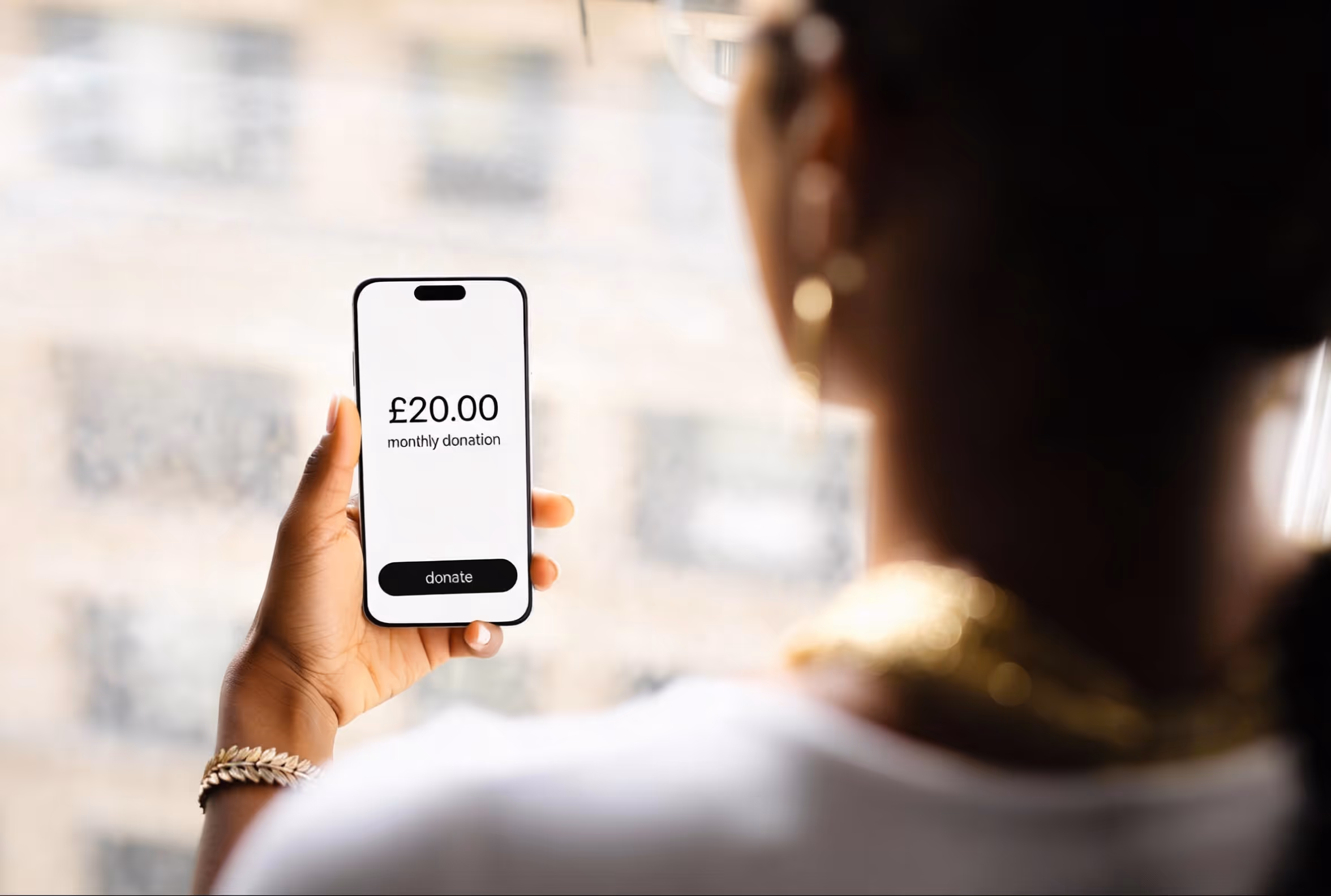 A person holds a phone displaying a £20.00 monthly donation screen with a "donate" button.