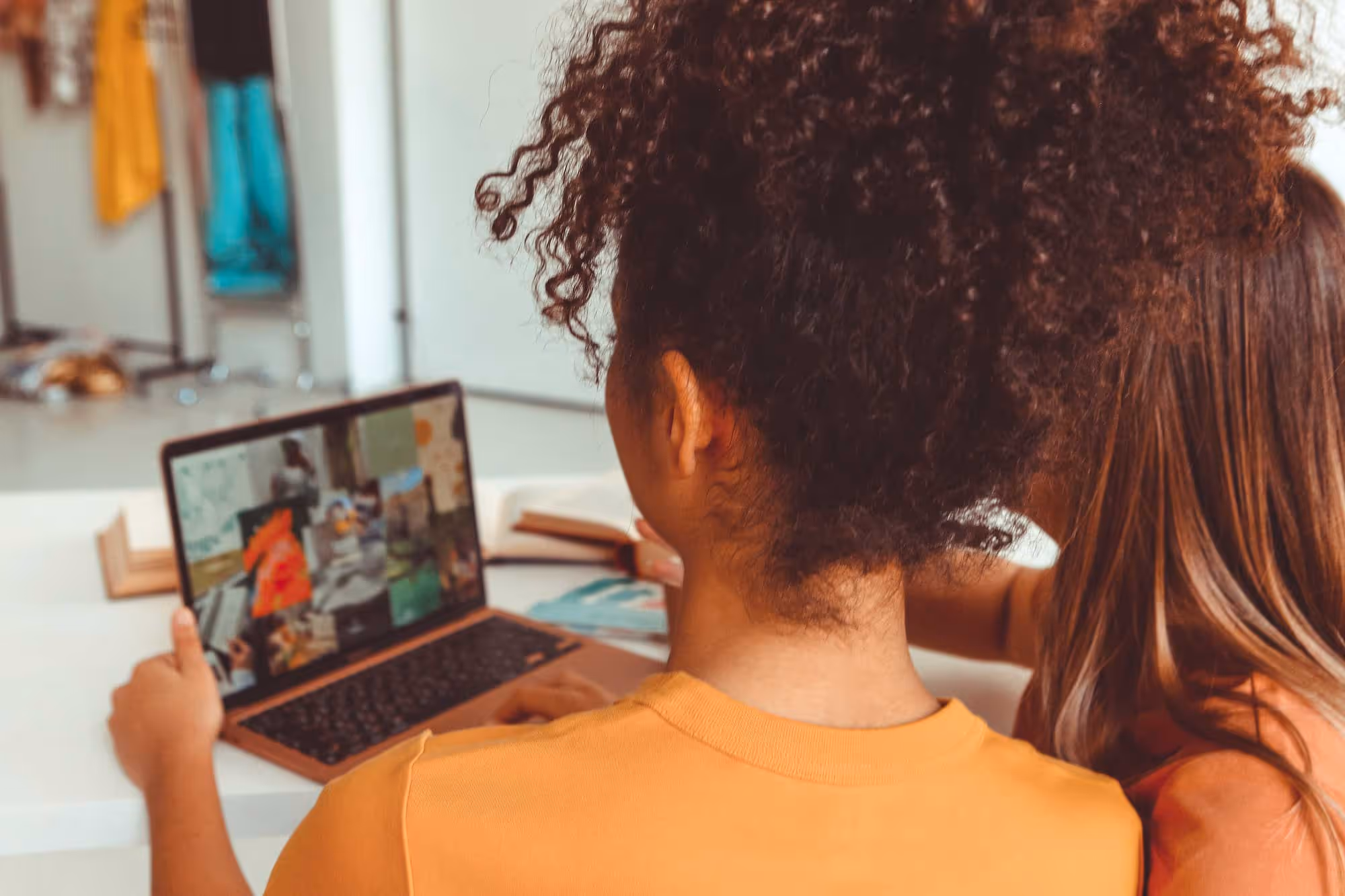 Two people sitting at a table, looking at a laptop screen displaying images.