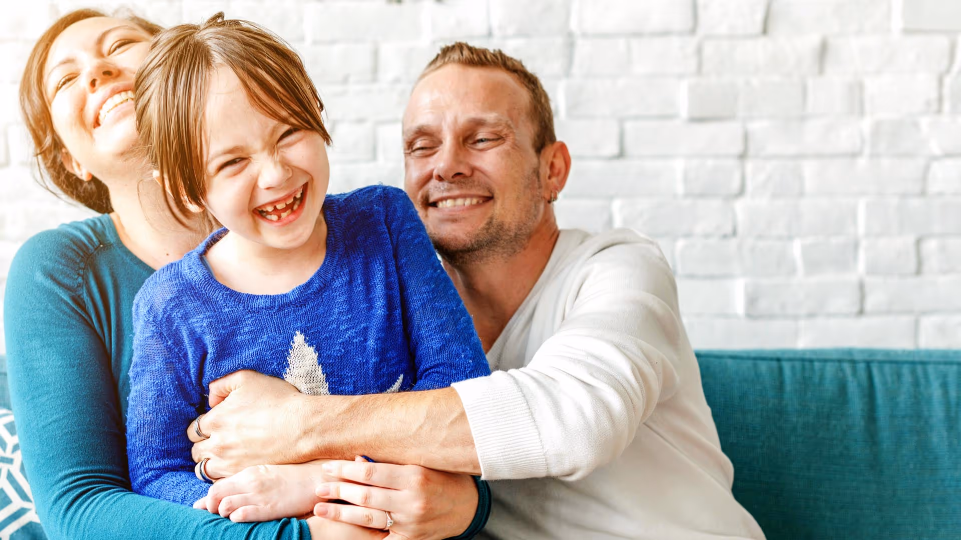 A family of three is sitting on a couch, smiling and hugging together warmly.
