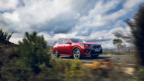 Roter BMW fährt durch eine grüne Landschaft bei bewölktem Himmel – MOTORHEIMAT Wagner-Schwarz in Kirchseeon, Traunstein, Altenmarkt, Wasserburg und Oberhaching
