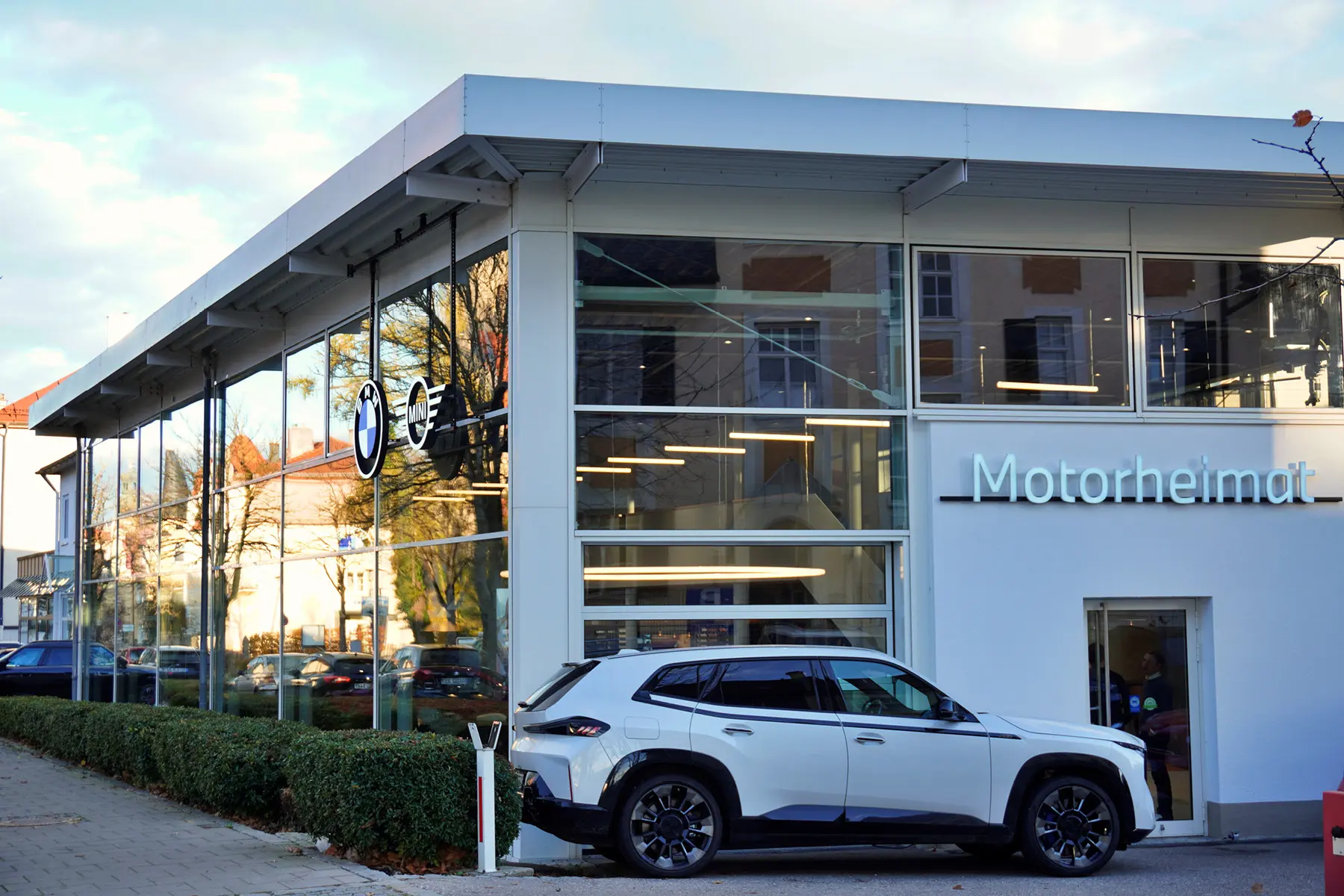 Weißer BMW XM vor dem Ausstellungsraum in Traunstein. weiße Fassade mit Glasfronten.