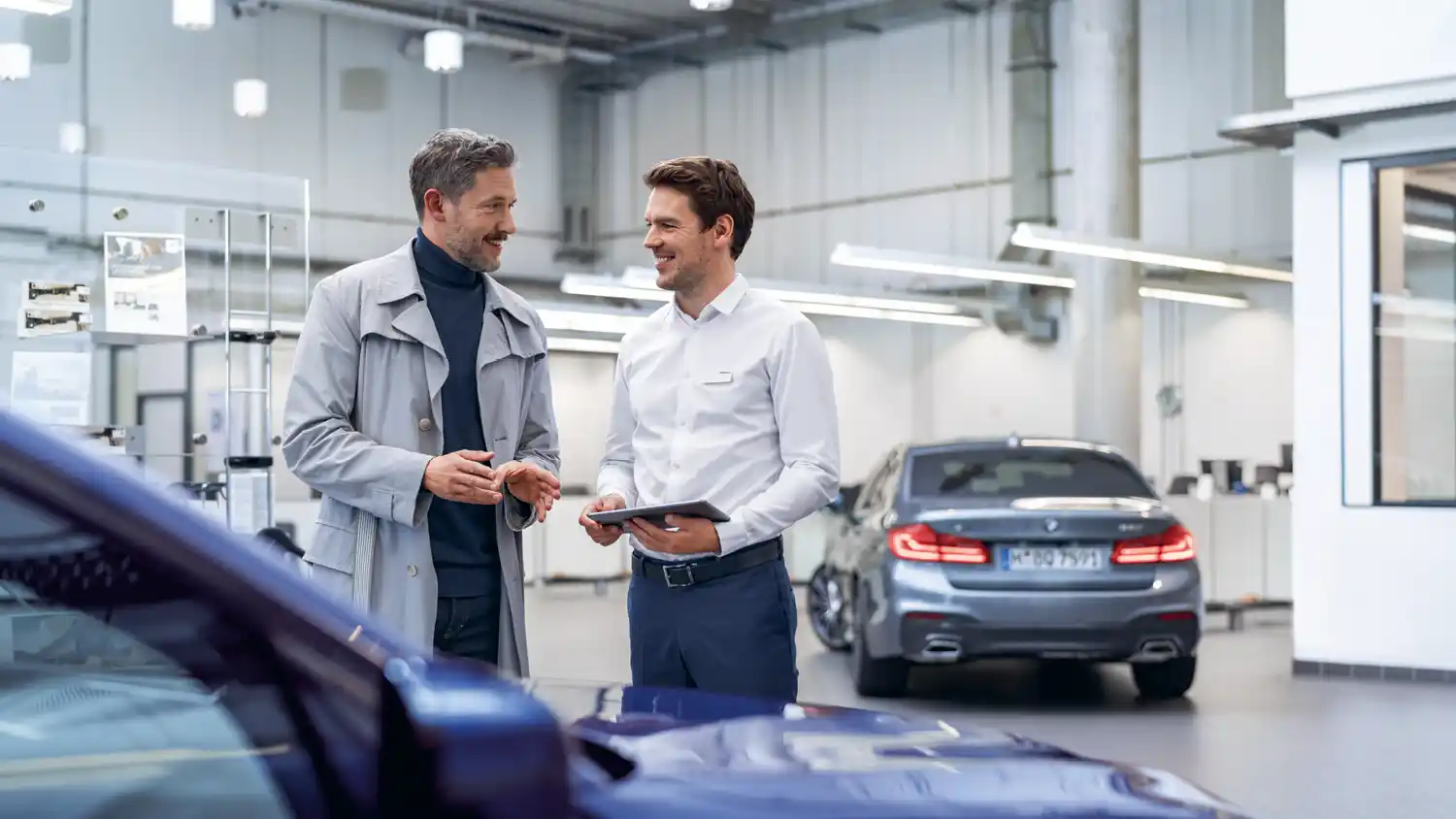 Männlicher Kunde und Mitarbeiter des Autohauses in Werkstatt bei der Service Annahme. 