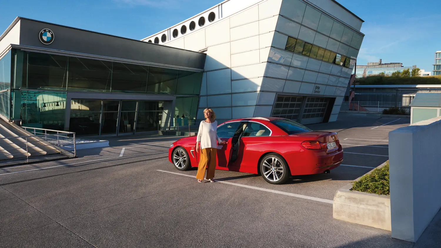 Roter BMW vor einem Autohaus. Frau steht vor dem Auto.