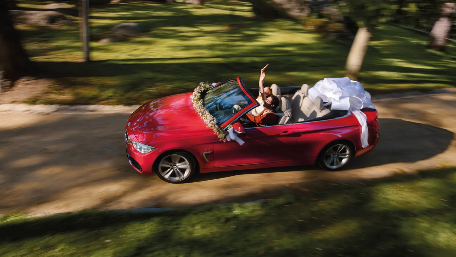 Rotes BMW 4er Cabrio mit Schleife fährt offen über einen Feldweg.