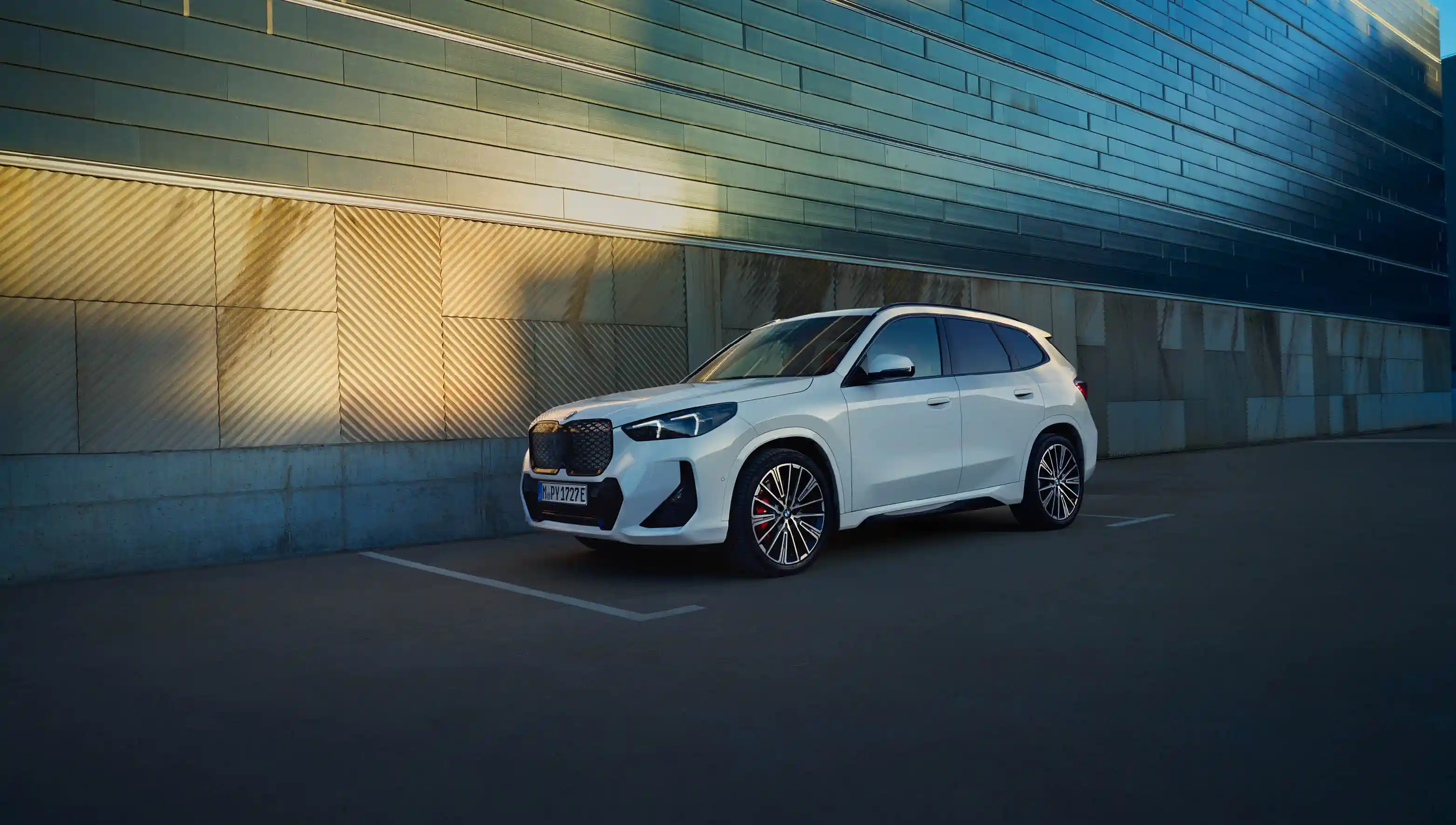 Weißer BMW iX1 vor einer Betonwand.