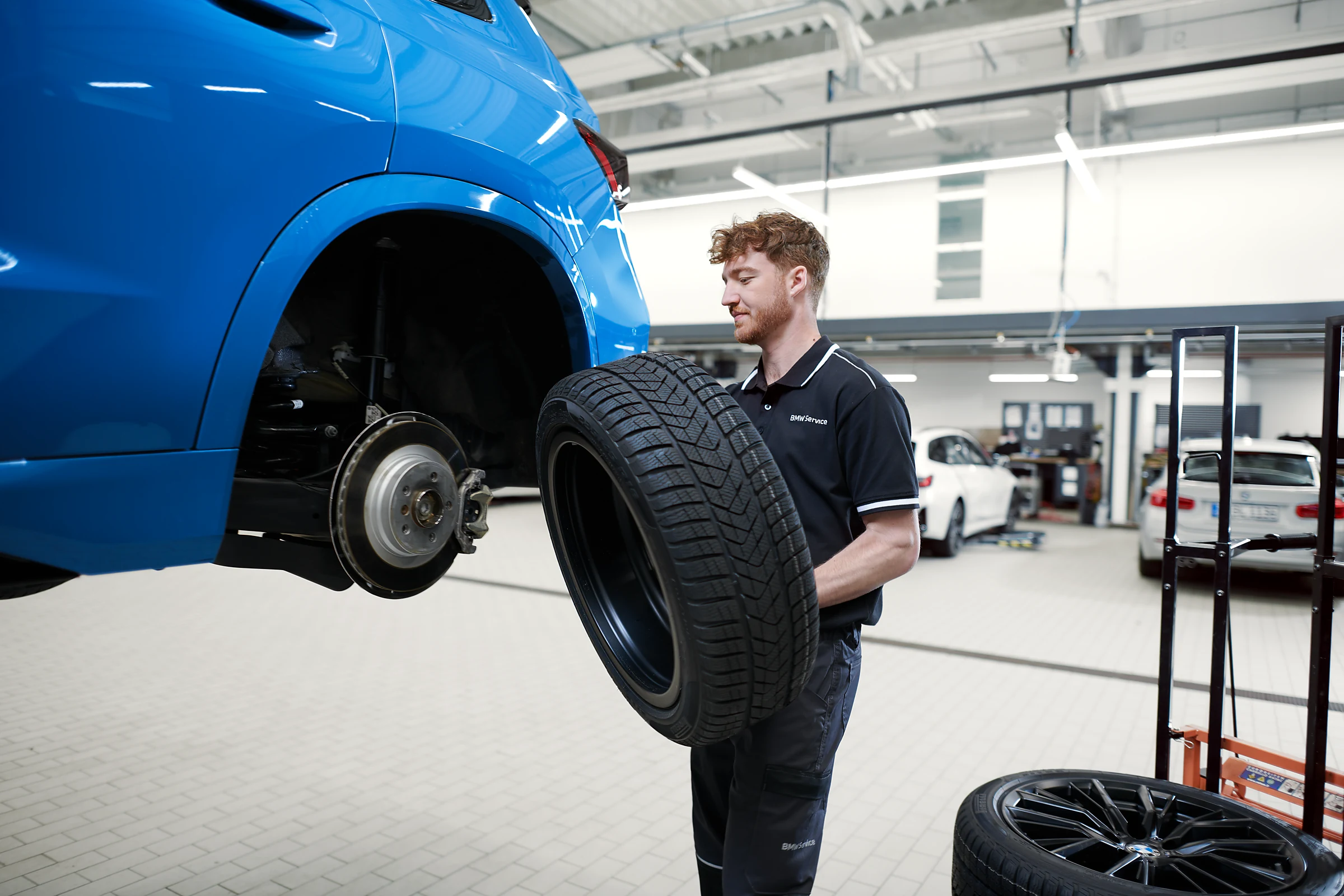 BMW Servicetechniker trägt Winterreifen zum aufgebockten BMW in der Werkstatt – MOTORHEIMAT Wagner-Schwarz in Kirchseeon, Traunstein, Altenmarkt, Wasserburg und Oberhaching