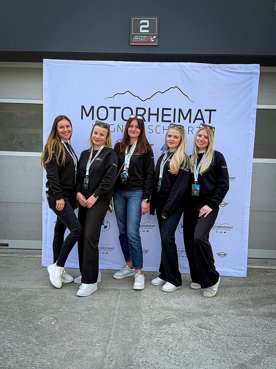 Mitarbeiterinnen der MOTORHEIMAT vor der Teamwand am Salzburgring – MOTORHEIMAT Wagner-Schwarz in Kirchseeon, Traunstein, Altenmarkt, Wasserburg und Oberhaching