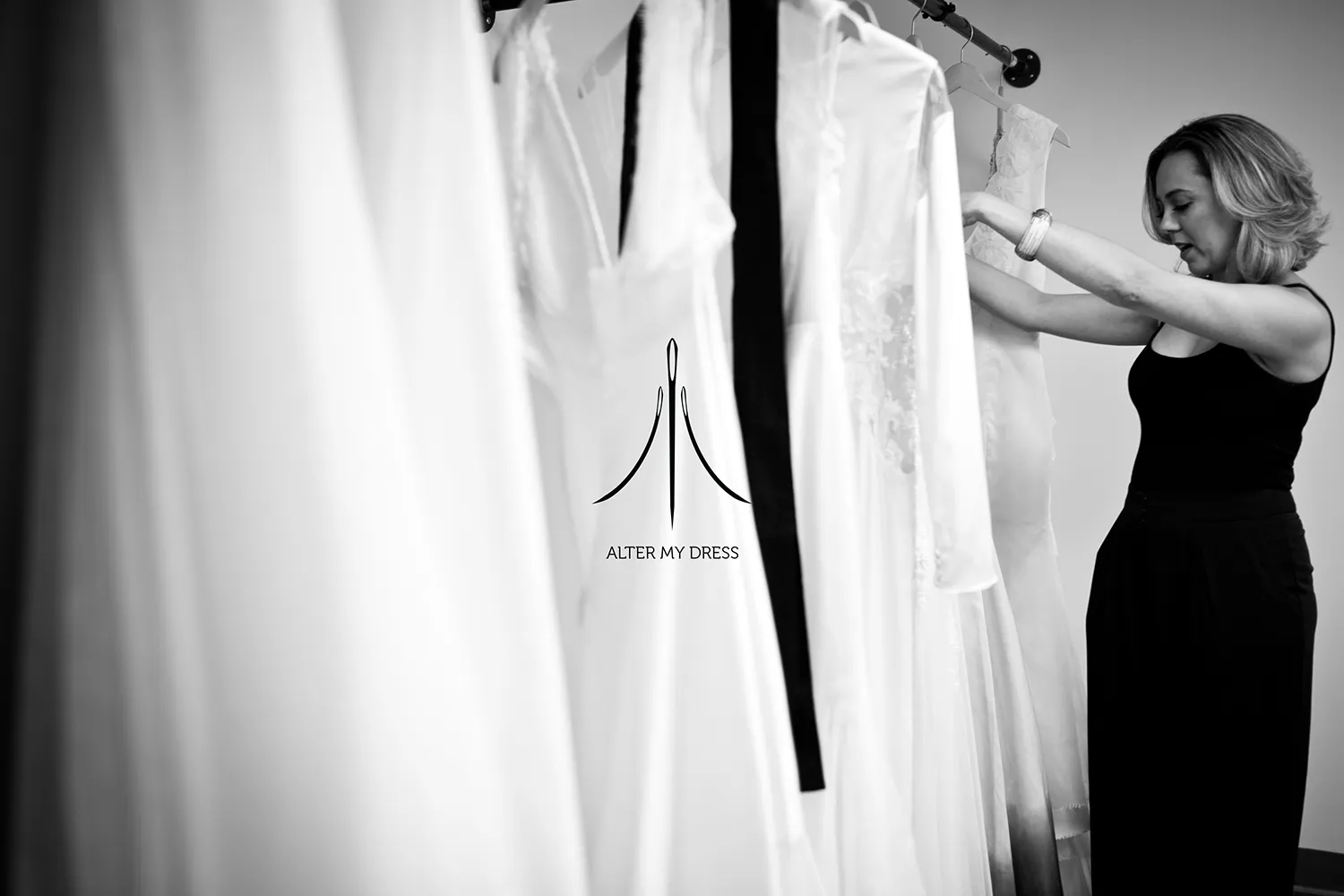 Alter My Dress logo on black and white background image of lead designer Priscilla looking through wedding dresses on a rack