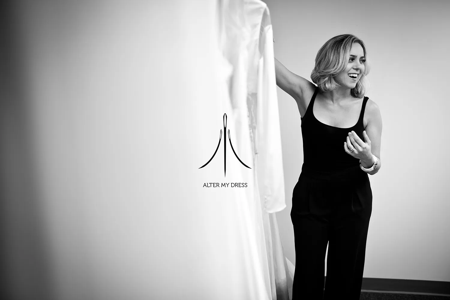 Fashion designer adjusting a sheer, beaded top and white tulle skirt worn by a model against a white background with Alter My Dress logo.
