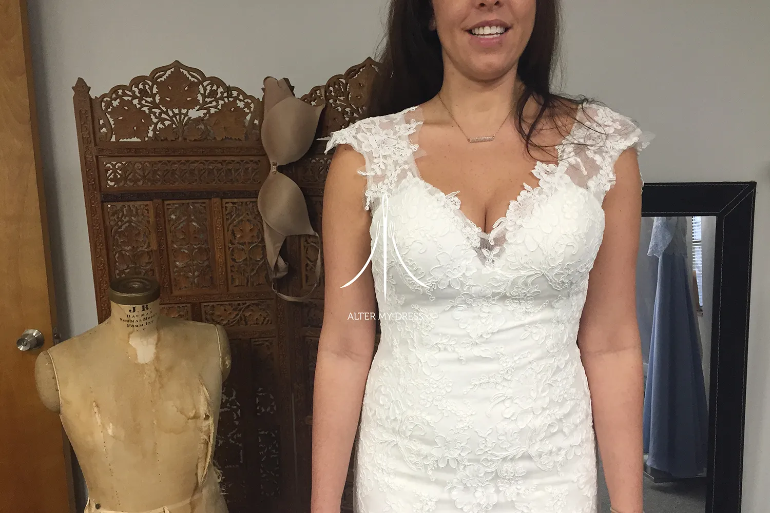 Fashion designer adjusting a sheer, beaded top and white tulle skirt worn by a model against a white background with Alter My Dress logo.