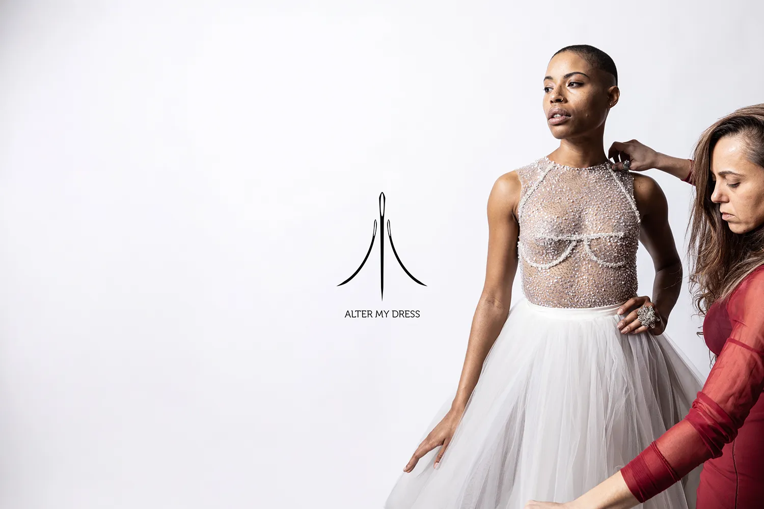 Fashion designer adjusting a sheer, beaded top and white tulle skirt worn by a model against a white background with Alter My Dress logo.