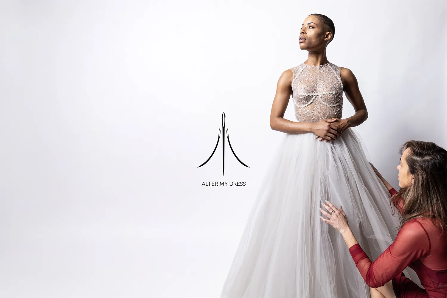 Designer adjusting the flowing tulle skirt of a sheer, beaded bodice wedding dress worn by a model.