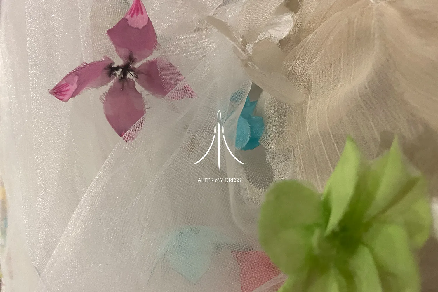 Delicate fabric with translucent white tulle decorated with pink, blue, and green floral appliqués.