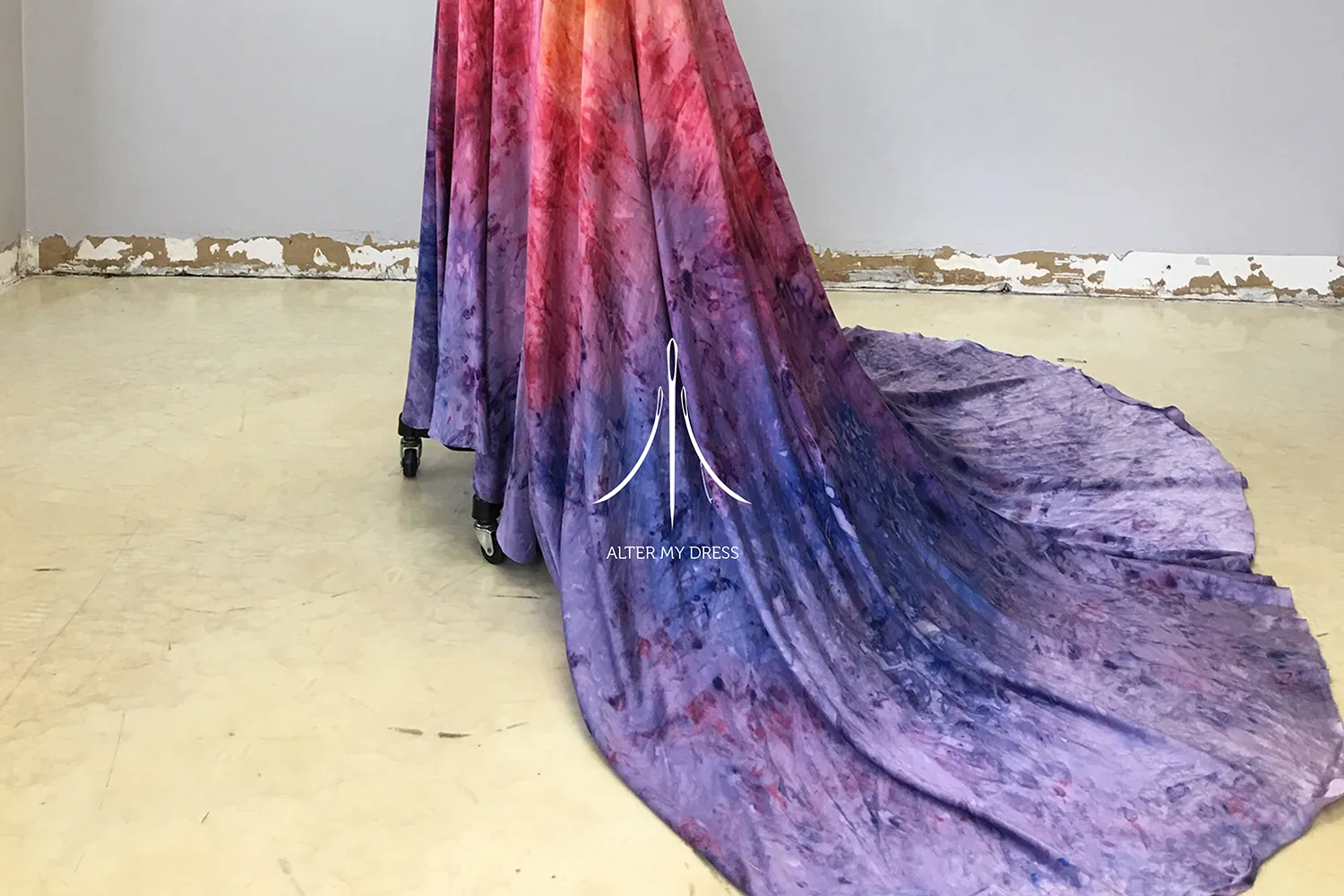 Flowing dress with a gradient tie-dye pattern in shades of purple, pink, and blue trailing on a beige floor.